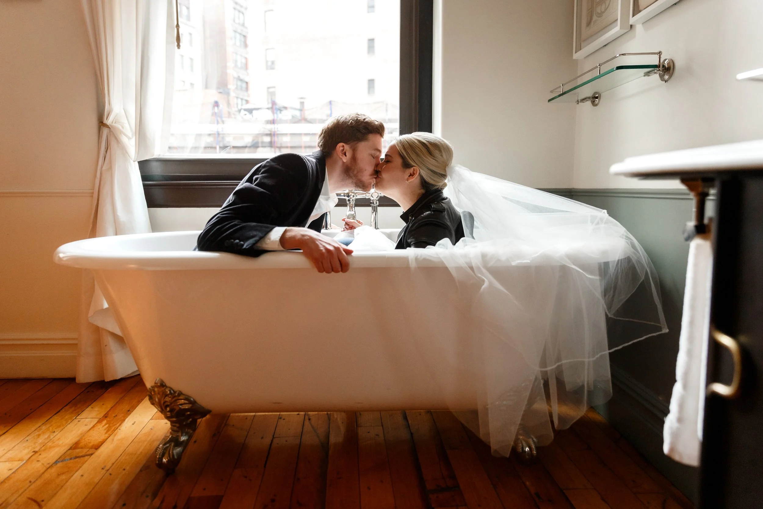 A newlywed couple kissing as they sit in a bathtub together 