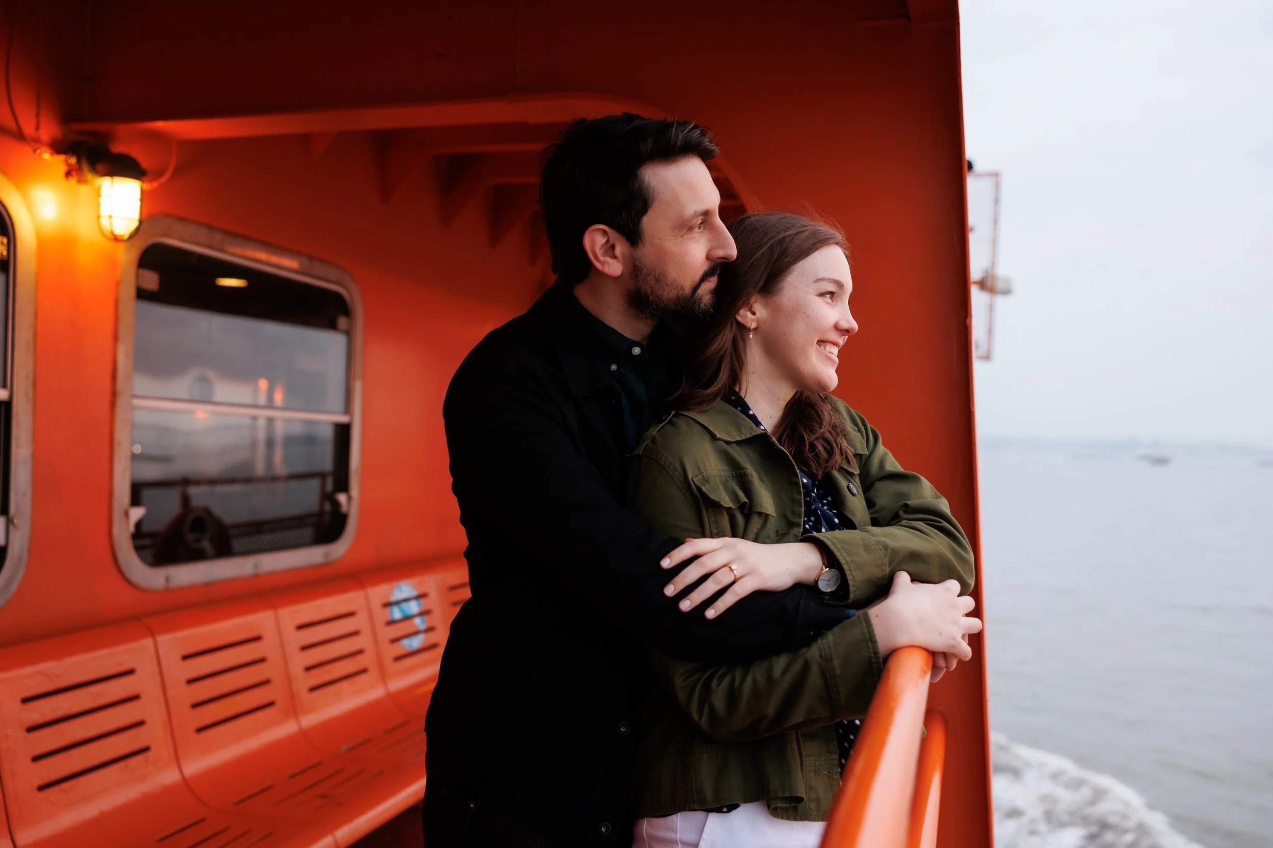 A person wrapping their partner up from behind as they stand at the railing on a ferry 
