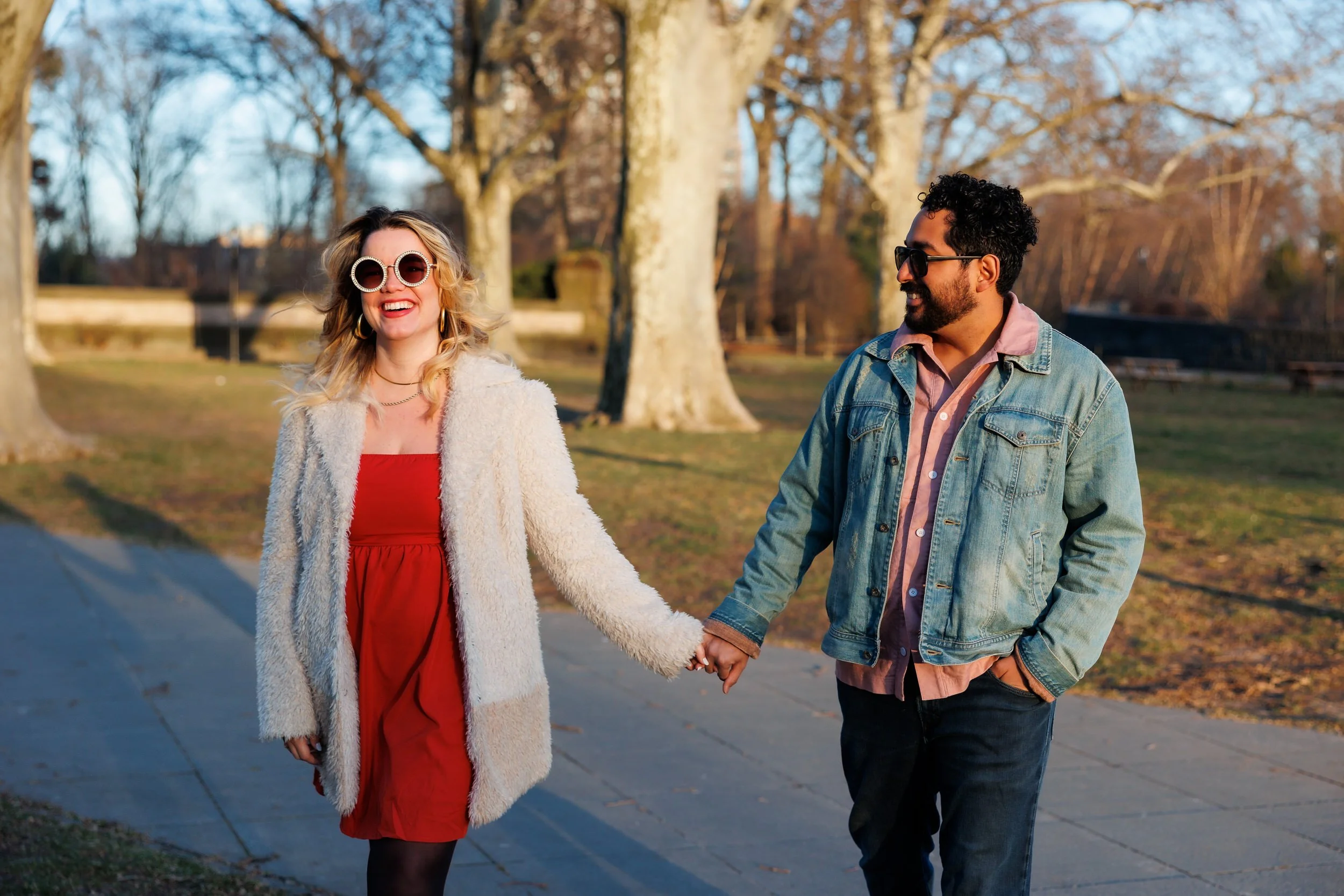 A couple in sunglasses holding hands and walking in a park 