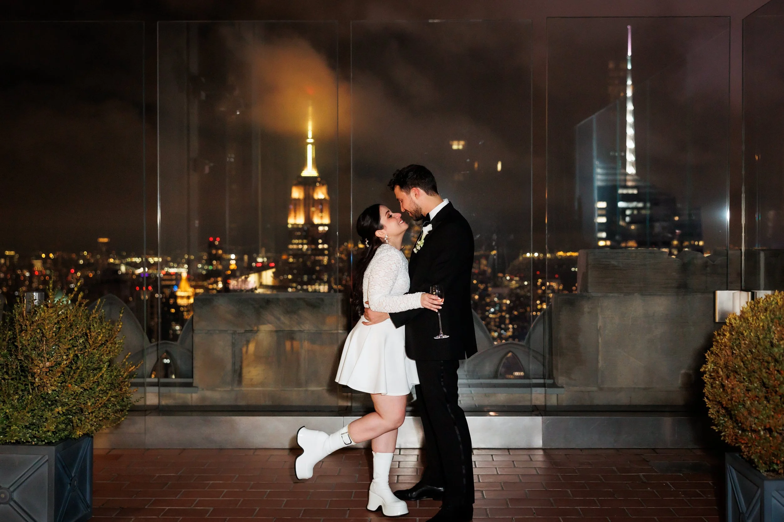 A wedding couple standing nose to nose with the city skyline behind them 