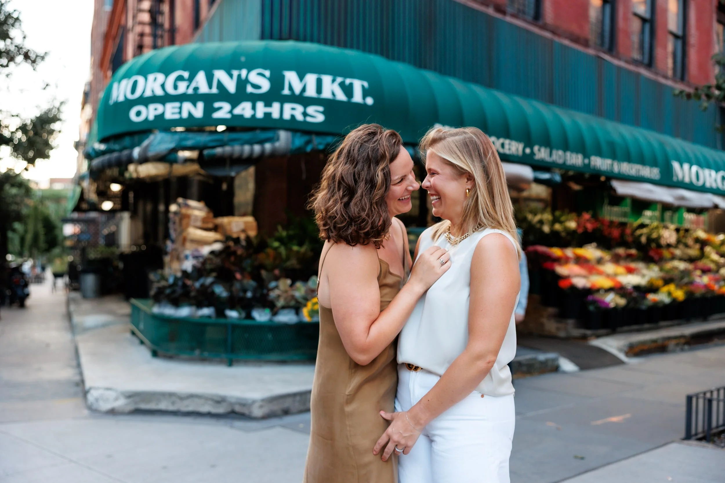 A couple standing close together as they lean in to kiss while standing on a city street corner 