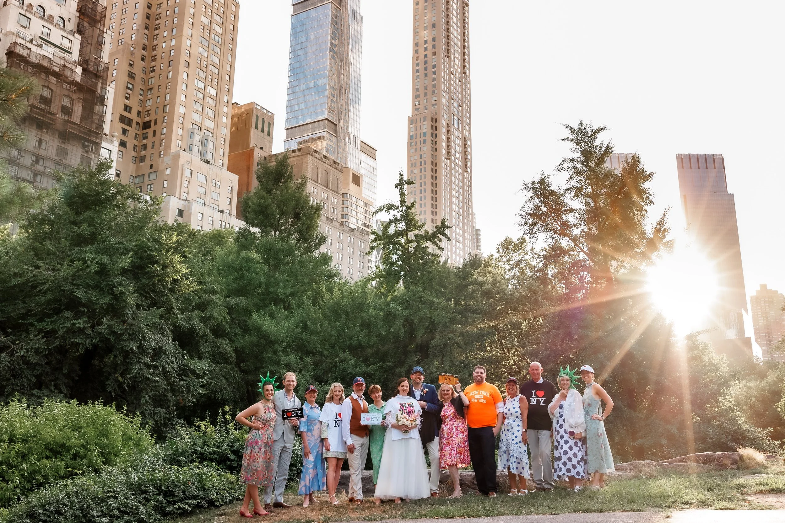 Newlyweds with their guests smiling together in a city park at sunset 