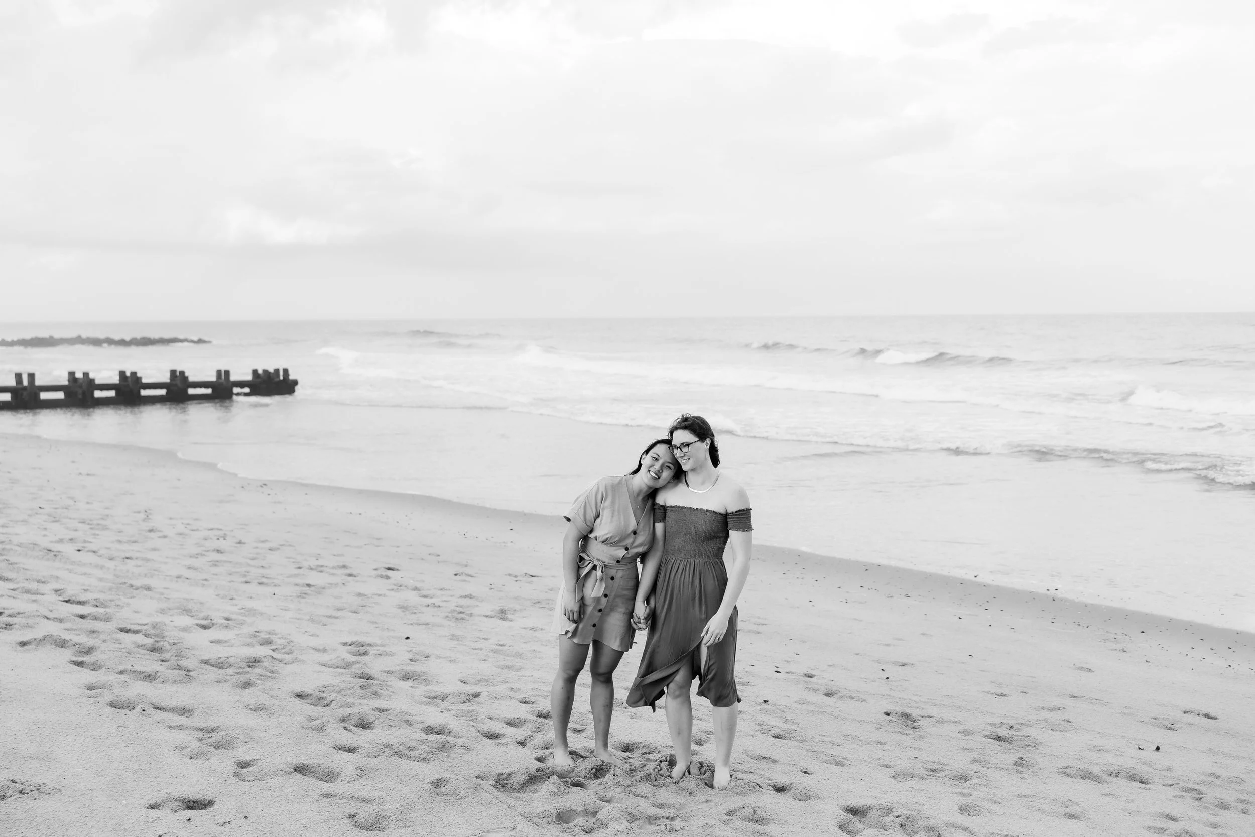 A person resting their head on their partner's shoulder as they stand on the water's edge 