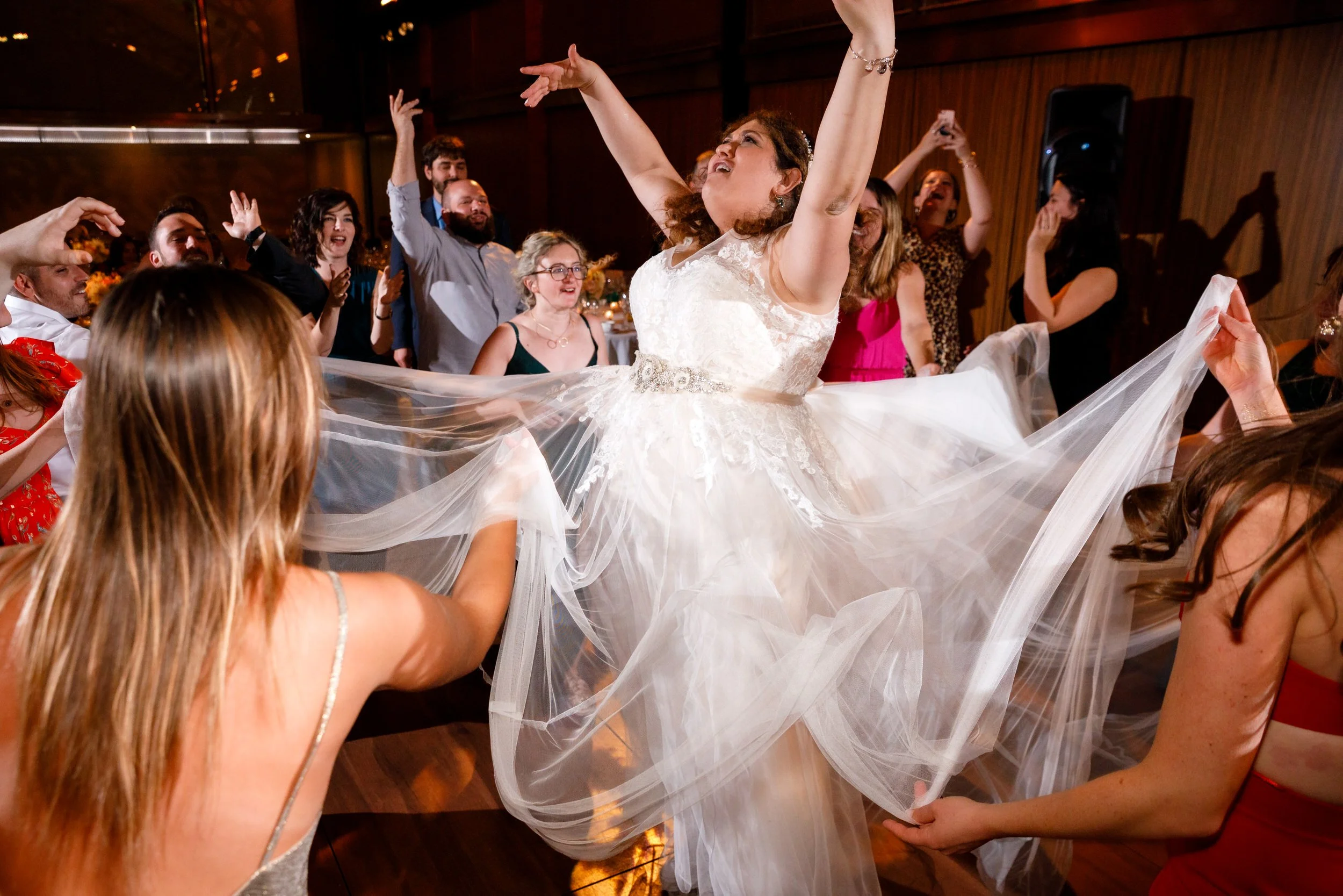 A newlywed dancing at their reception as guests hold out the train of their dress 