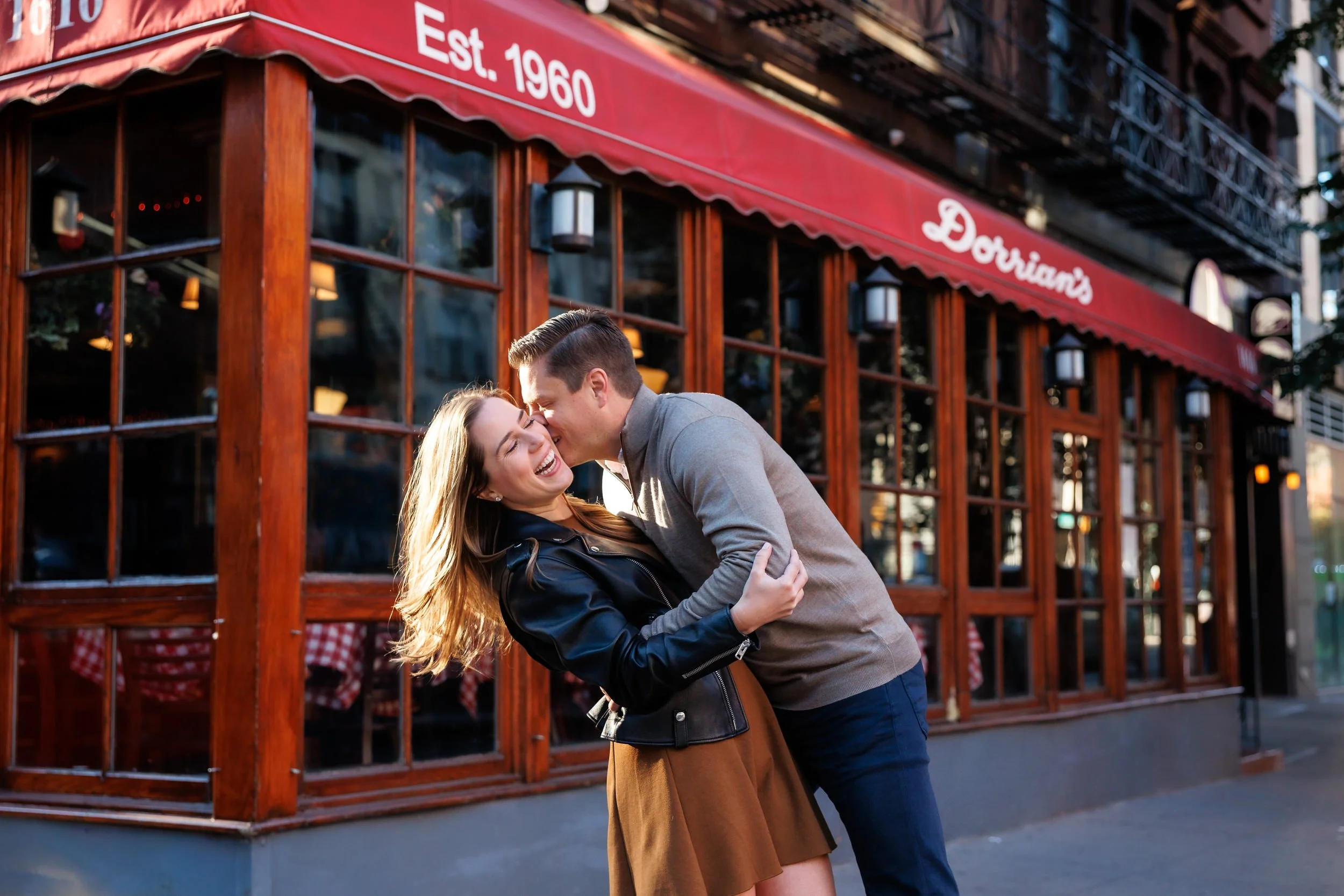 A person slightly dipping their partner and kissing their cheek as they laugh 