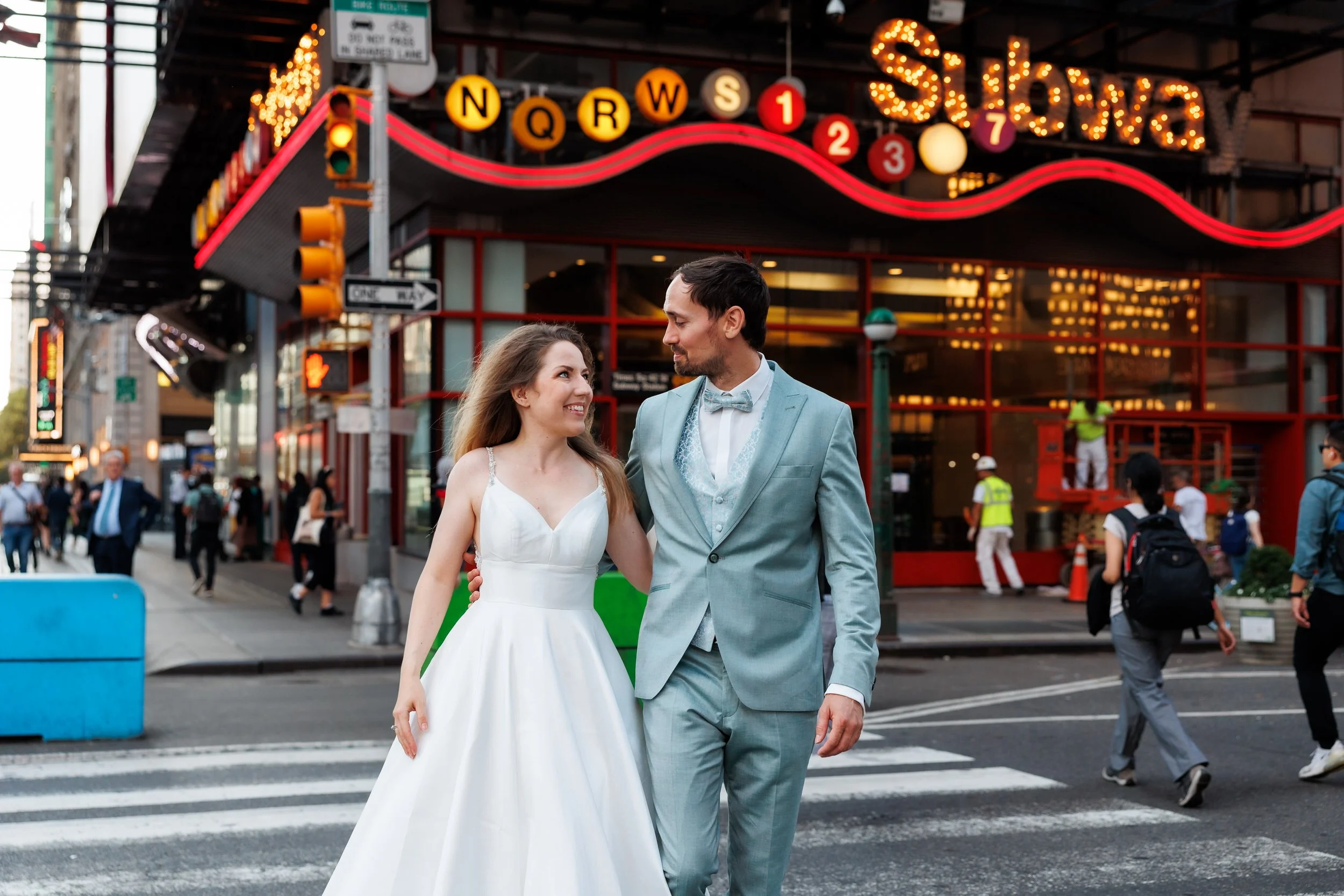A wedding couple walking with their arms around each other across a city crosswalk 