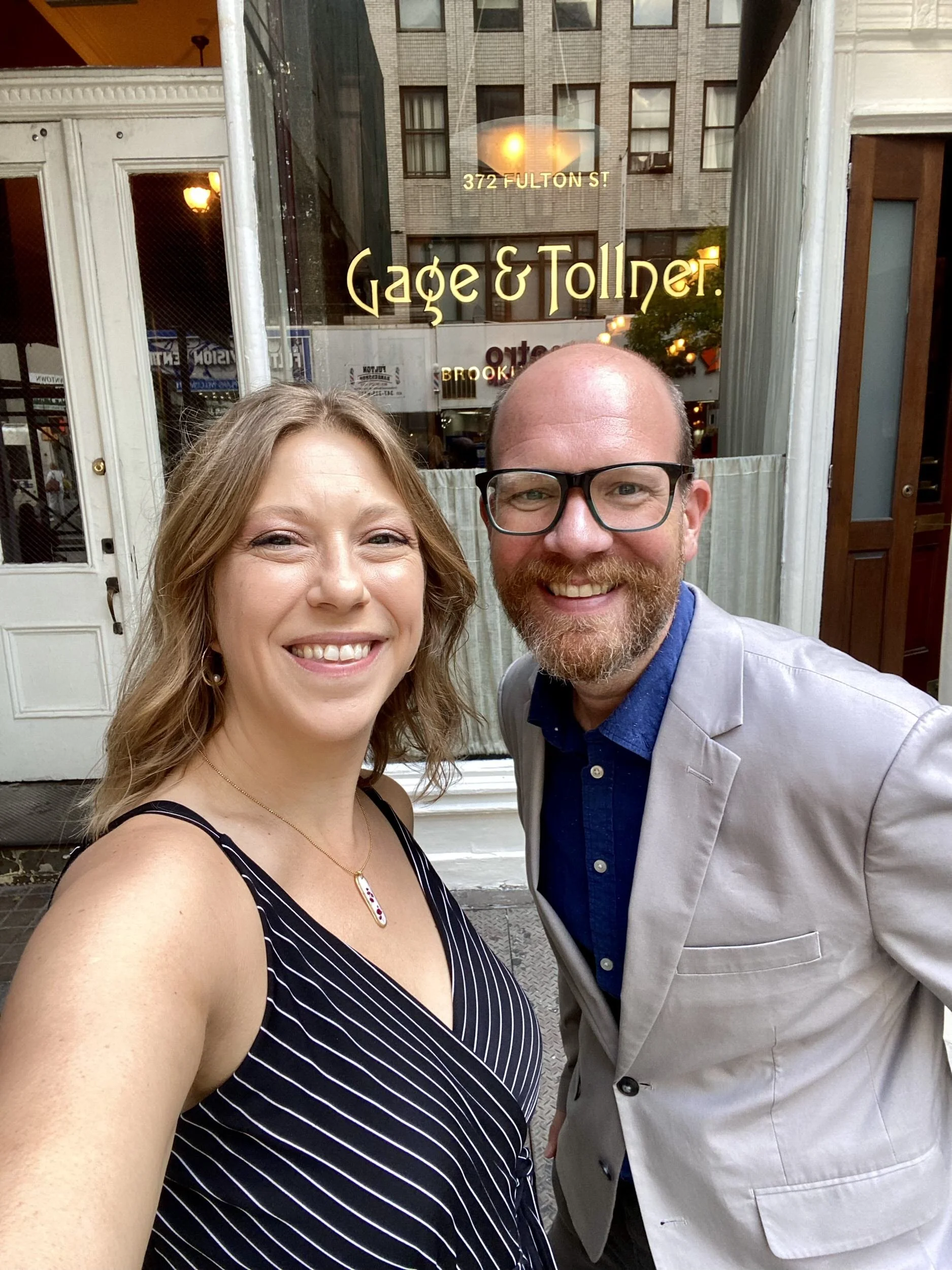 A couple smiling as they take a selfie in front of a restaurant