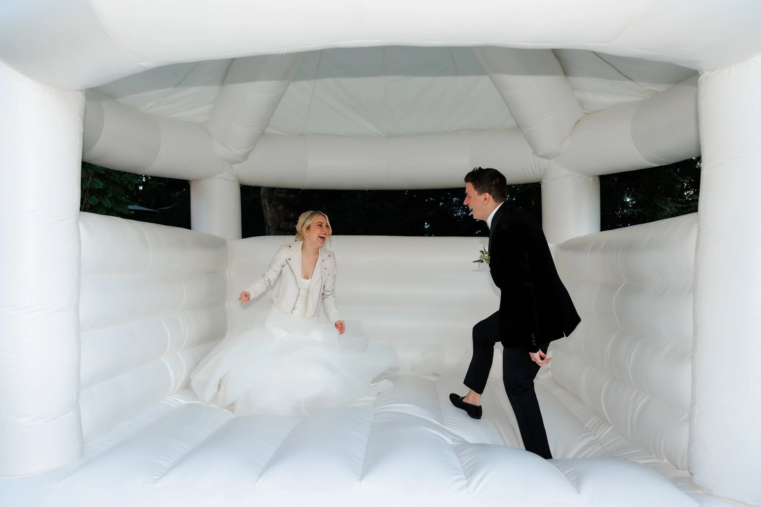 A wedding couple bouncing in a white bounce house 