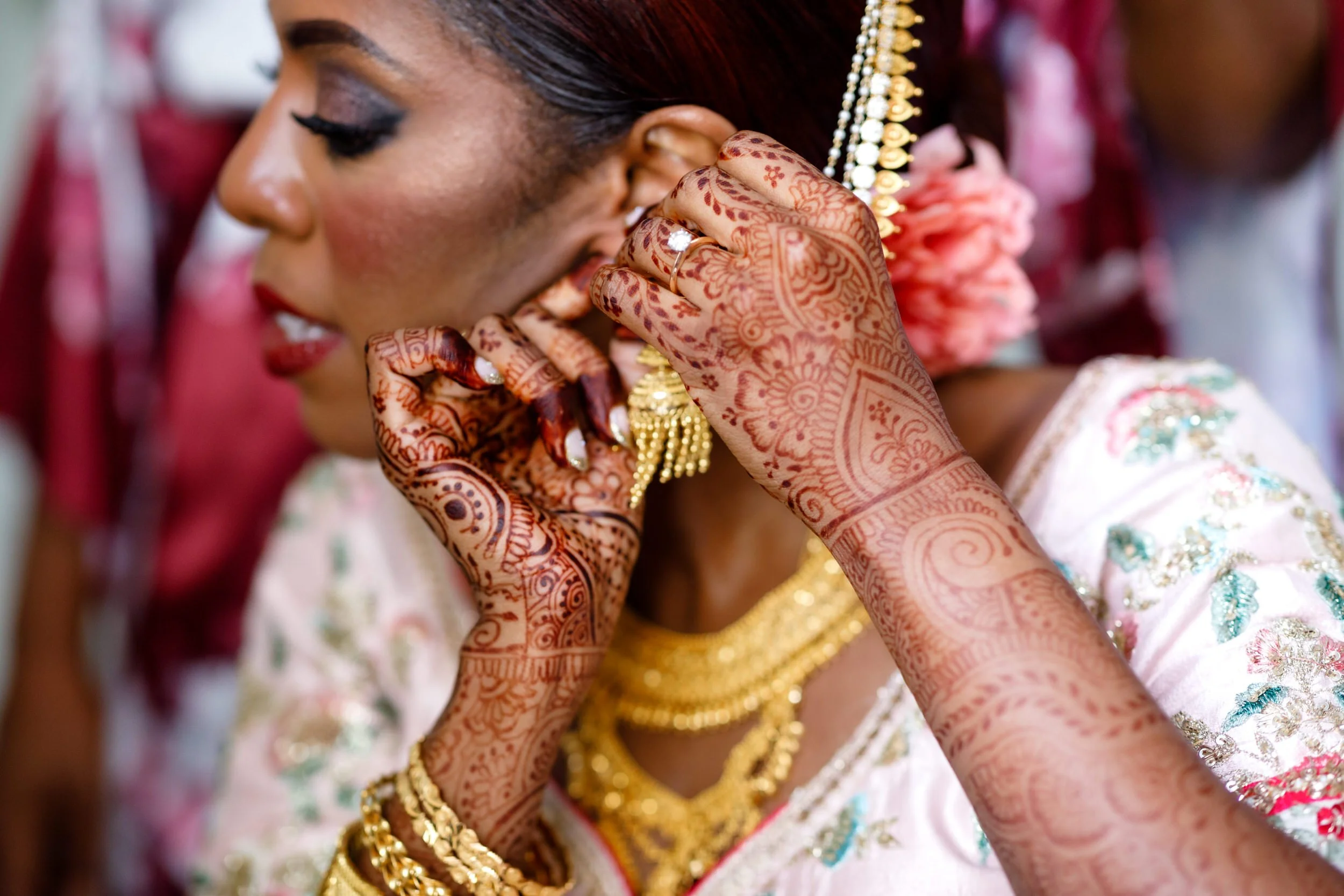 A person with henna tattoos on their arms putting on earrings 