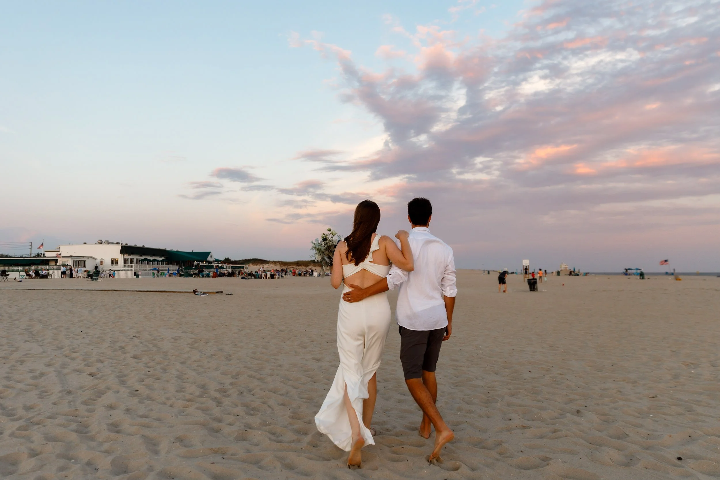 A newlywed couple with their arms around each other walking along the beach 