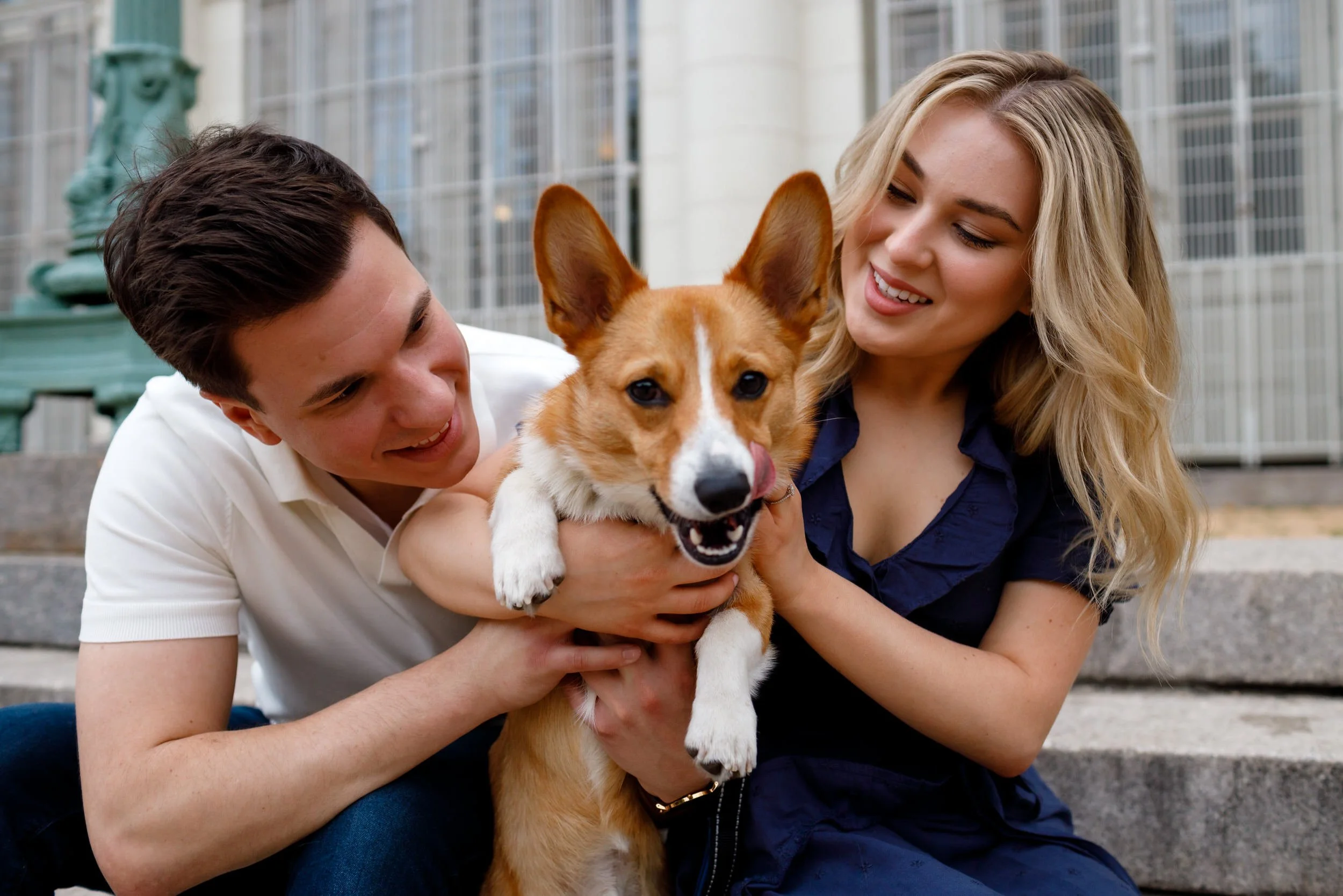 A couple smiling and holding a corgi in between them 