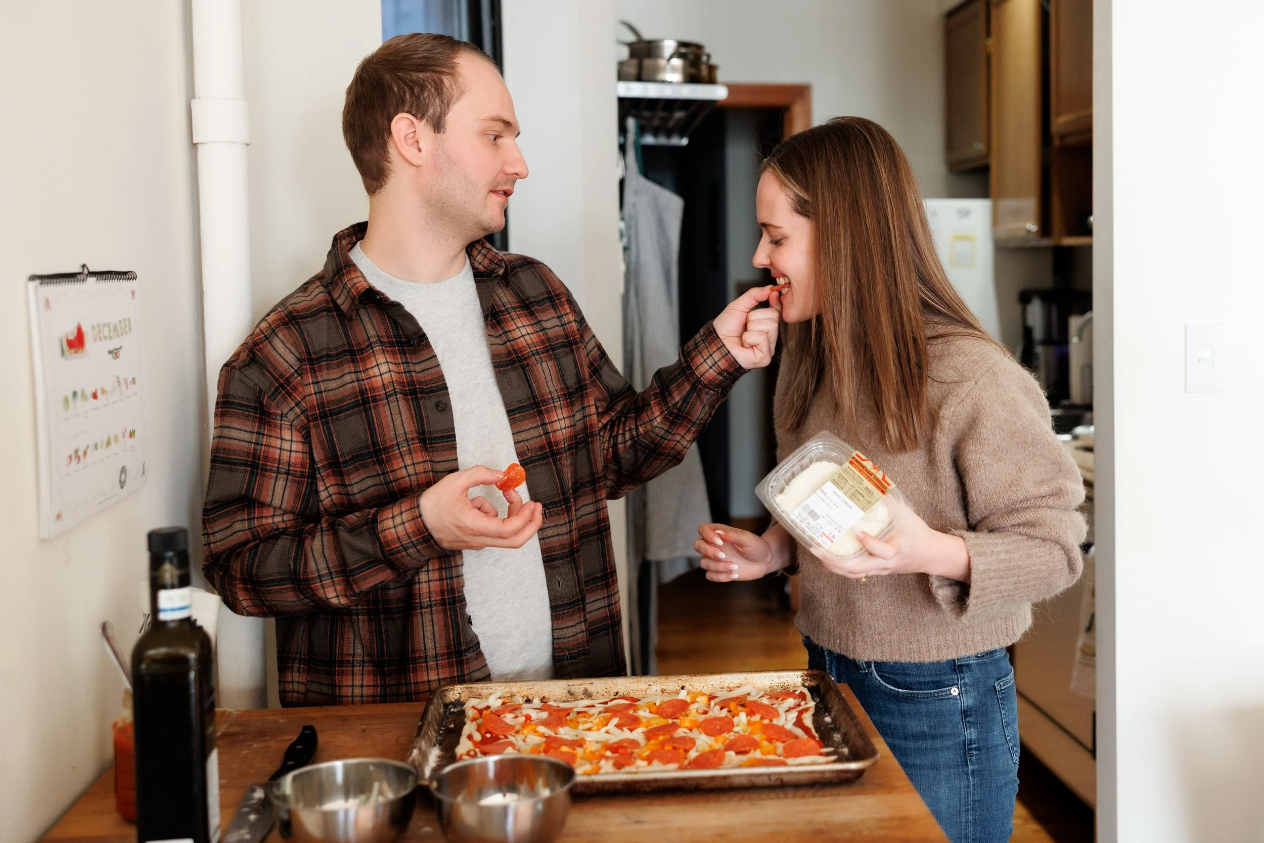 A person feeding their partner as they make a pizza together 