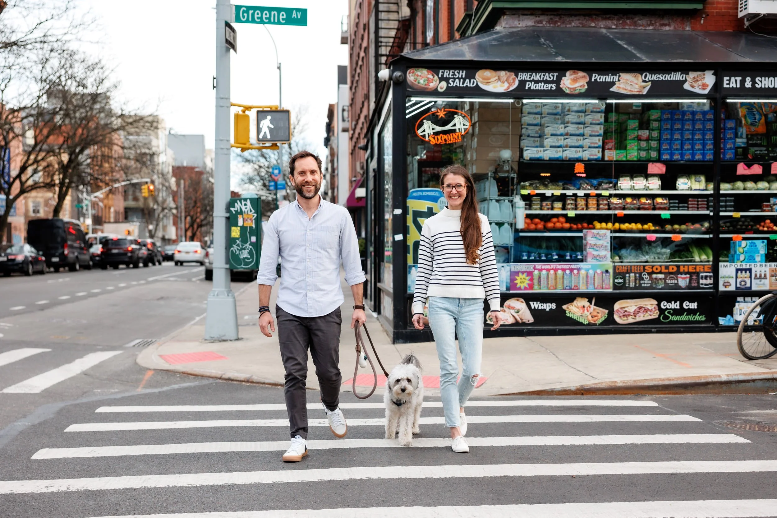 A couple walking across a crosswalk as one walks a dog between them 