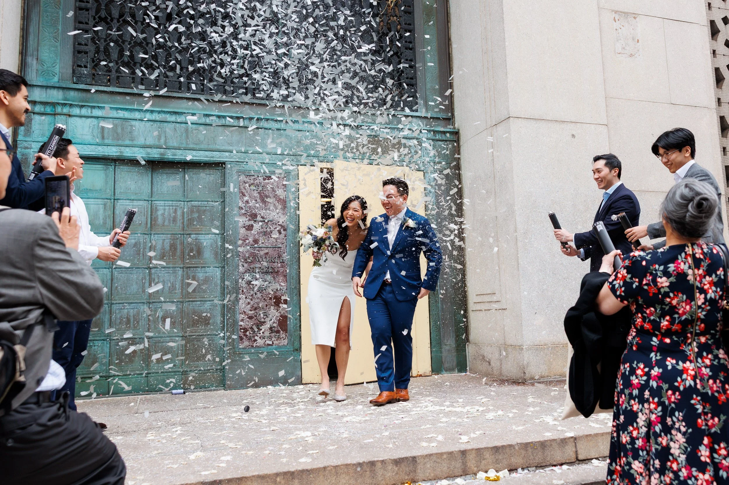 Wedding guests popping confetti as newlyweds laugh and walk through it