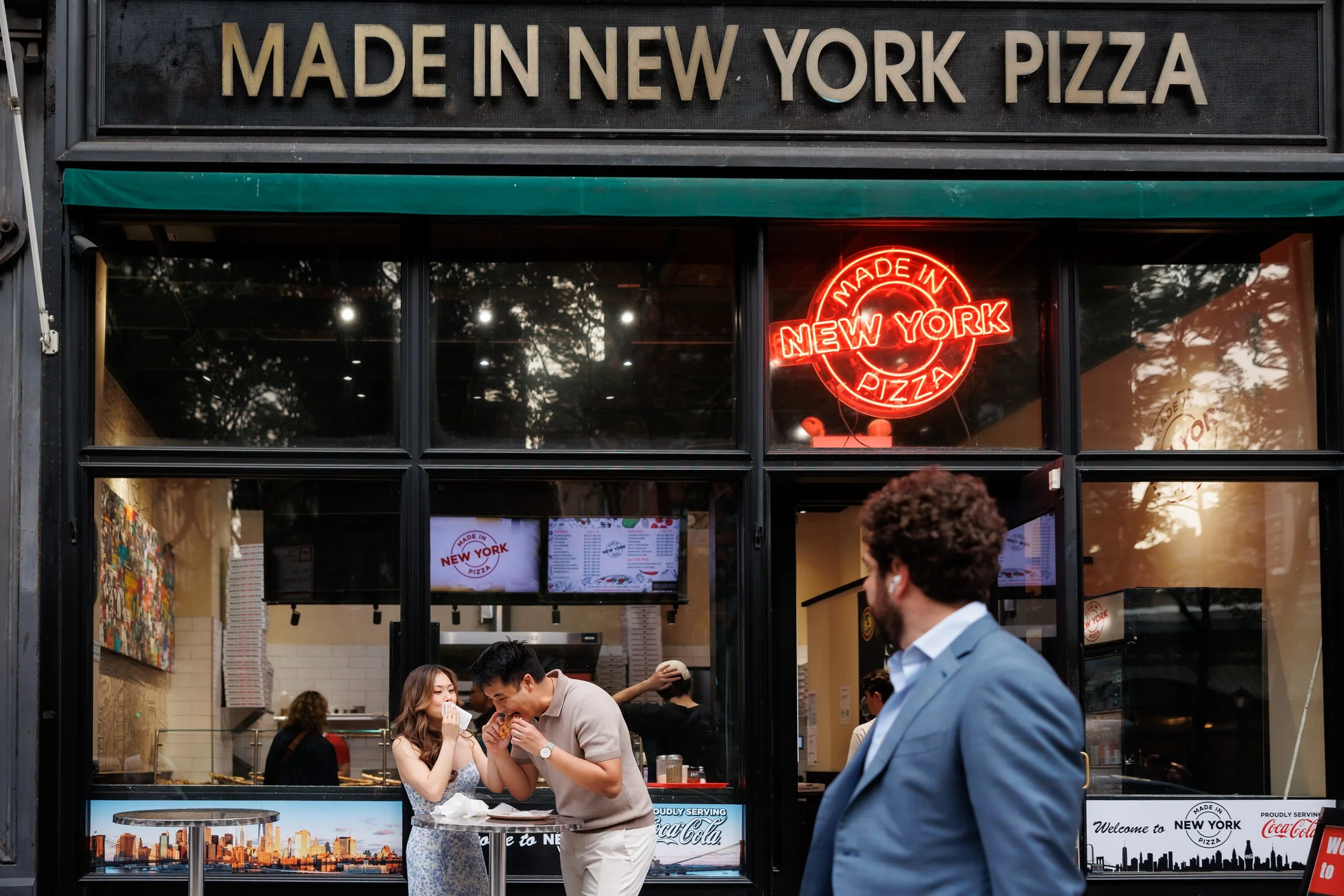 A couple eating pizza together at a standing table outside a New York pizzeria