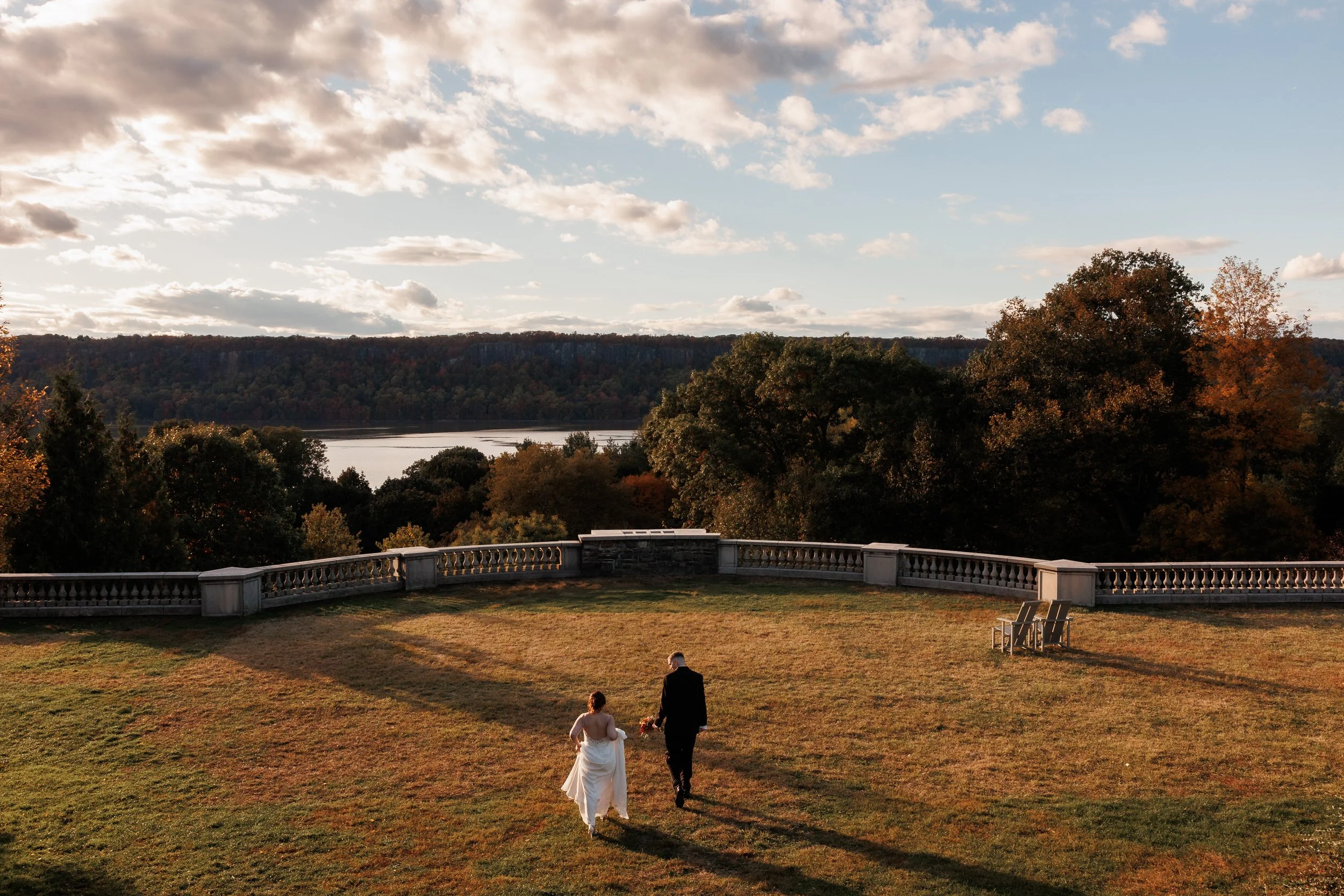 A wedding couple walking in a large field overlooking a lake 