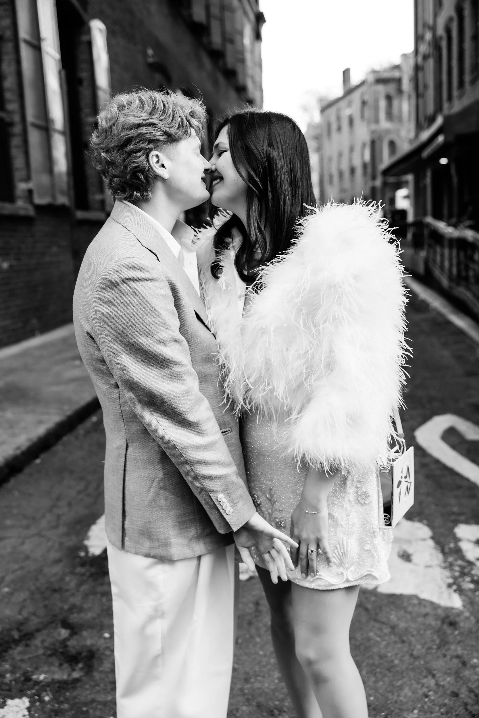 A couple holding hands as they lean in to kiss in an alleyway 