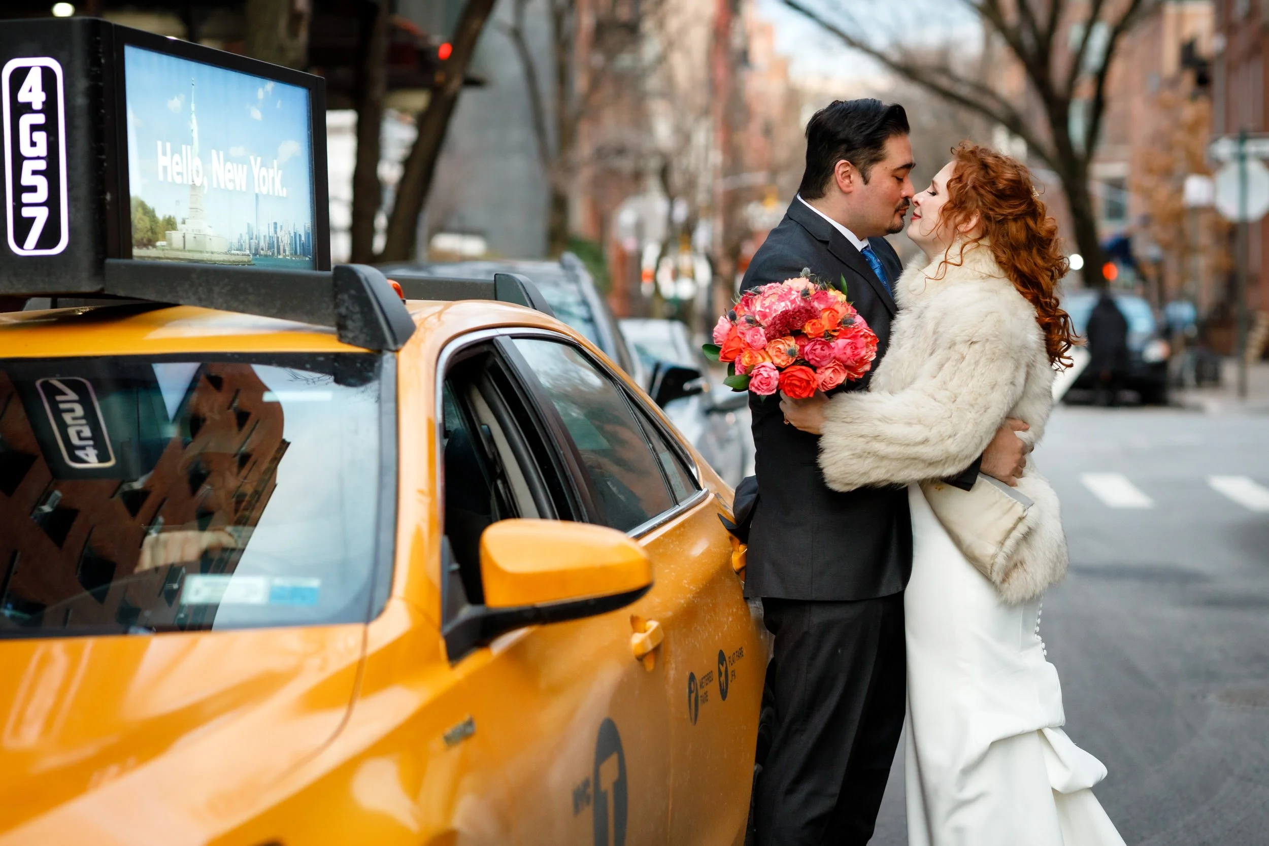 Newlyweds leaning into each other about to kiss as they stand next to a taxi on a city street