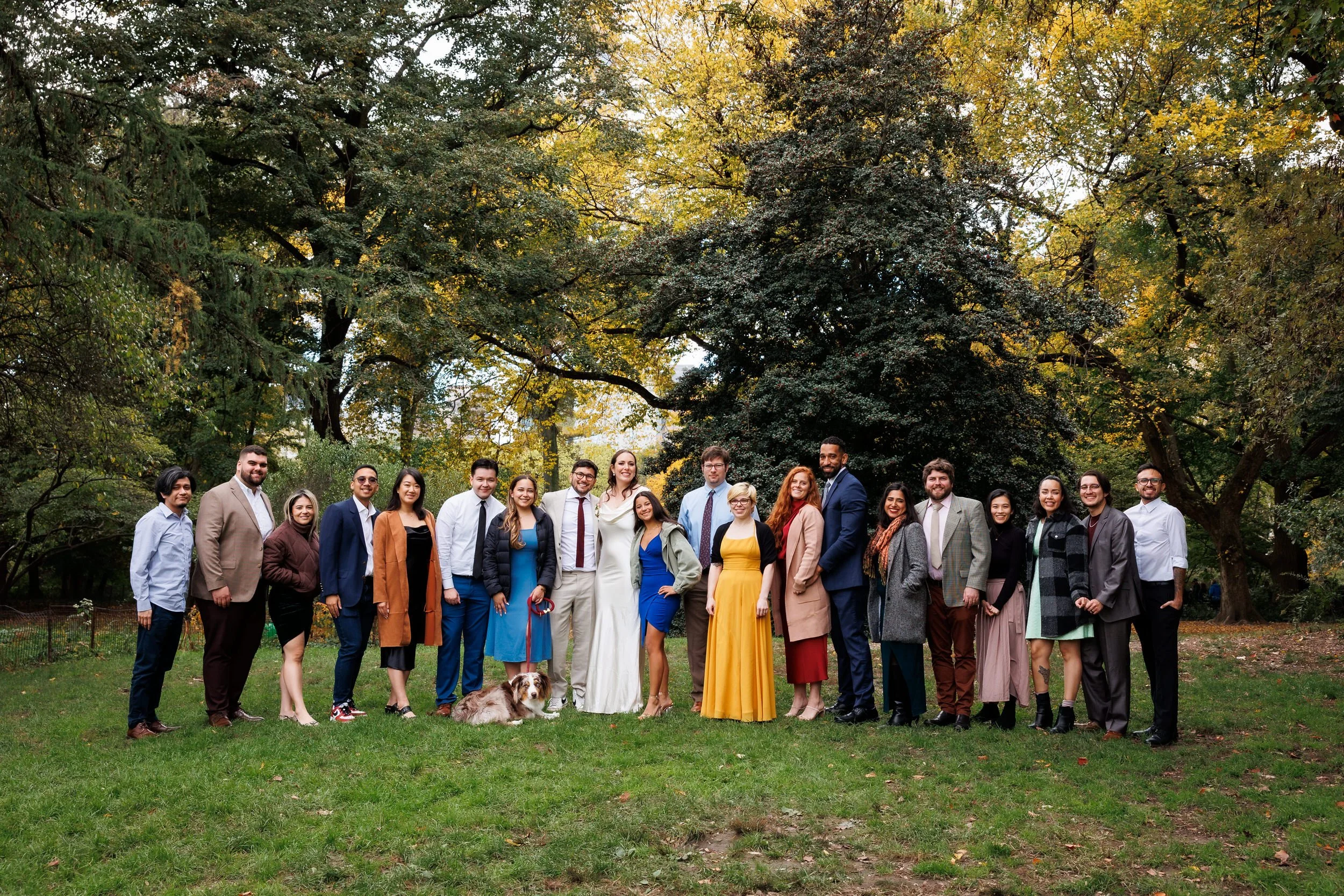 Newlyweds and their guests smiling while standing together in a wooded area 