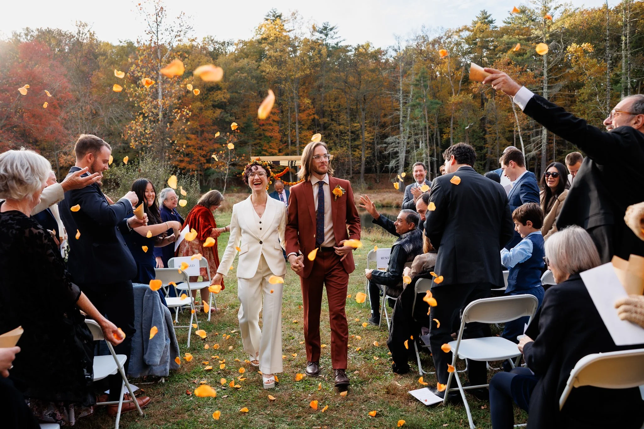 Couple walks up aisle after outdoor fall ceremony as guests throw marigold petals