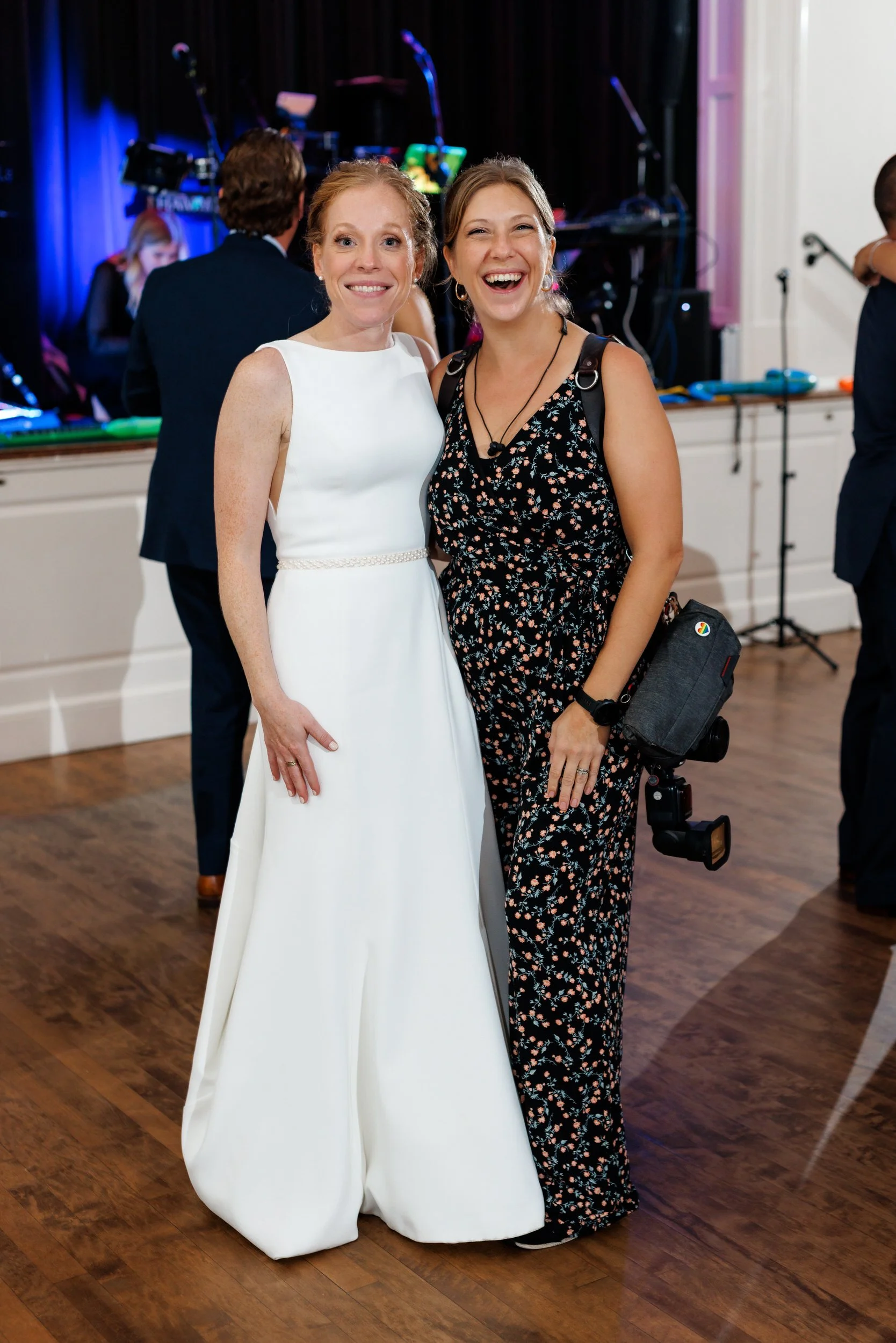 A photographer and a newlywed standing together smiling at a wedding reception