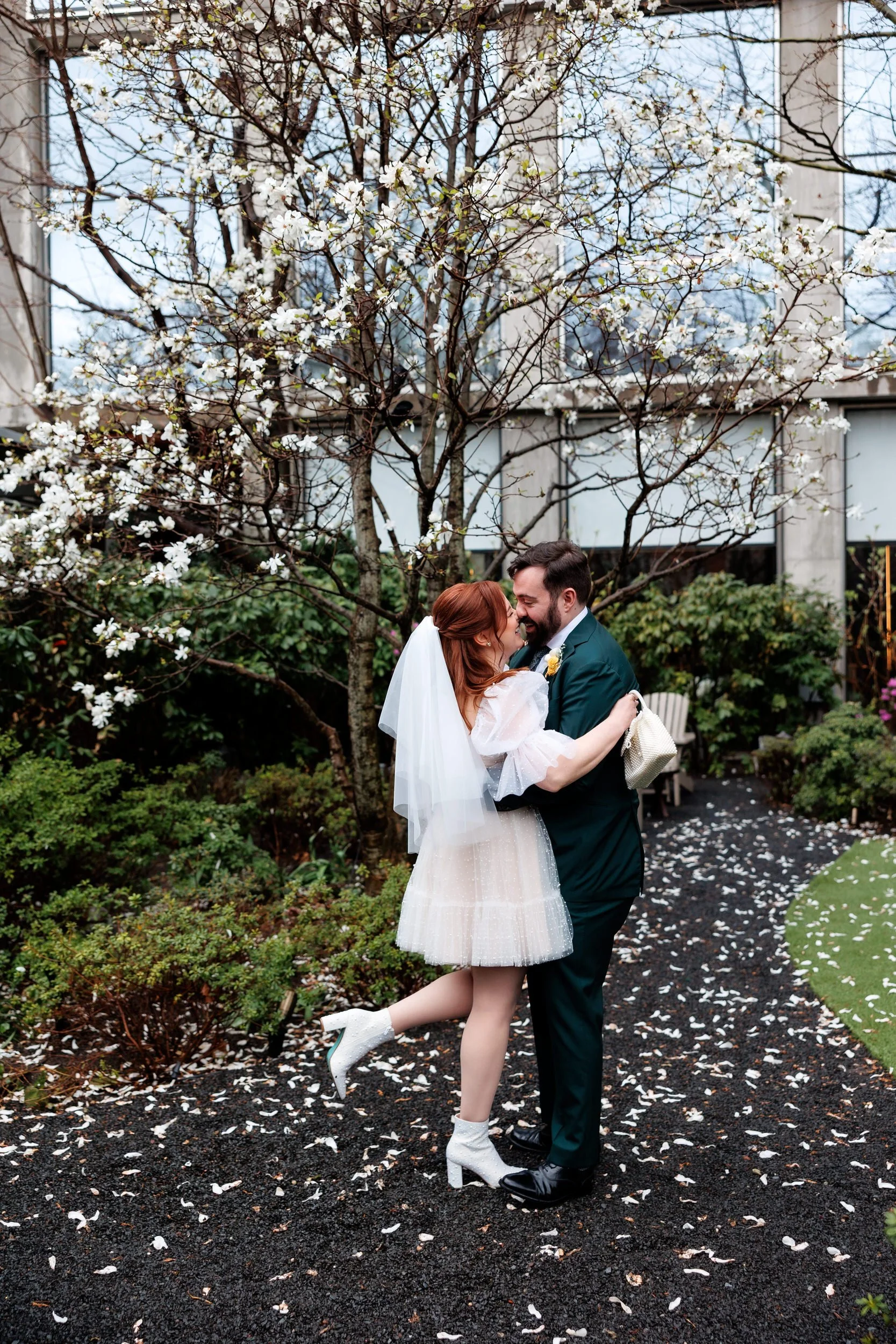 A newlywed couple about to kiss in a small garden area 