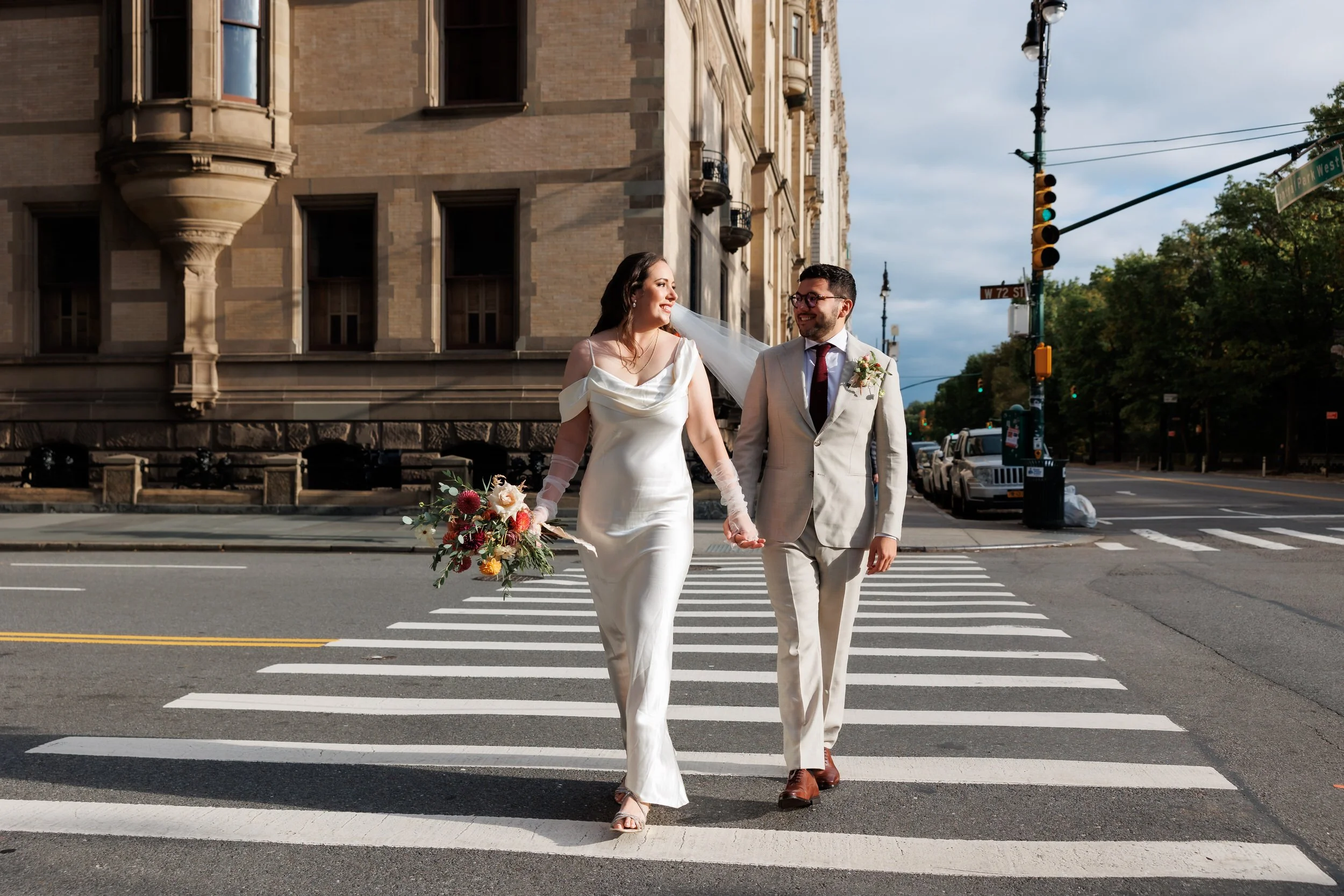 A newlywed couple holding hands and walking across a crosswalk 