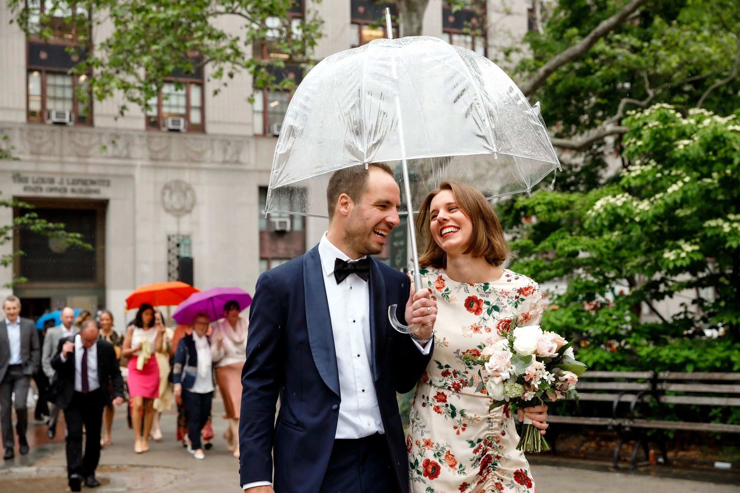 Newlyweds laughing as they walk together under a clear umbrella 