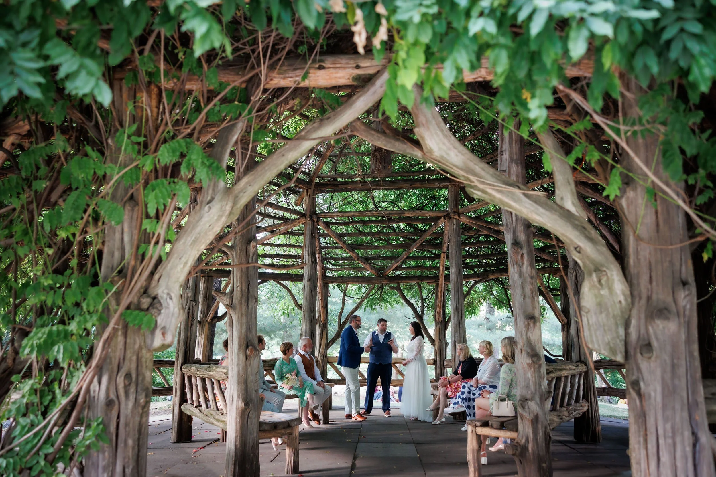 A couple exchanging vows with a handful of guests under a nature inspired gazebo 