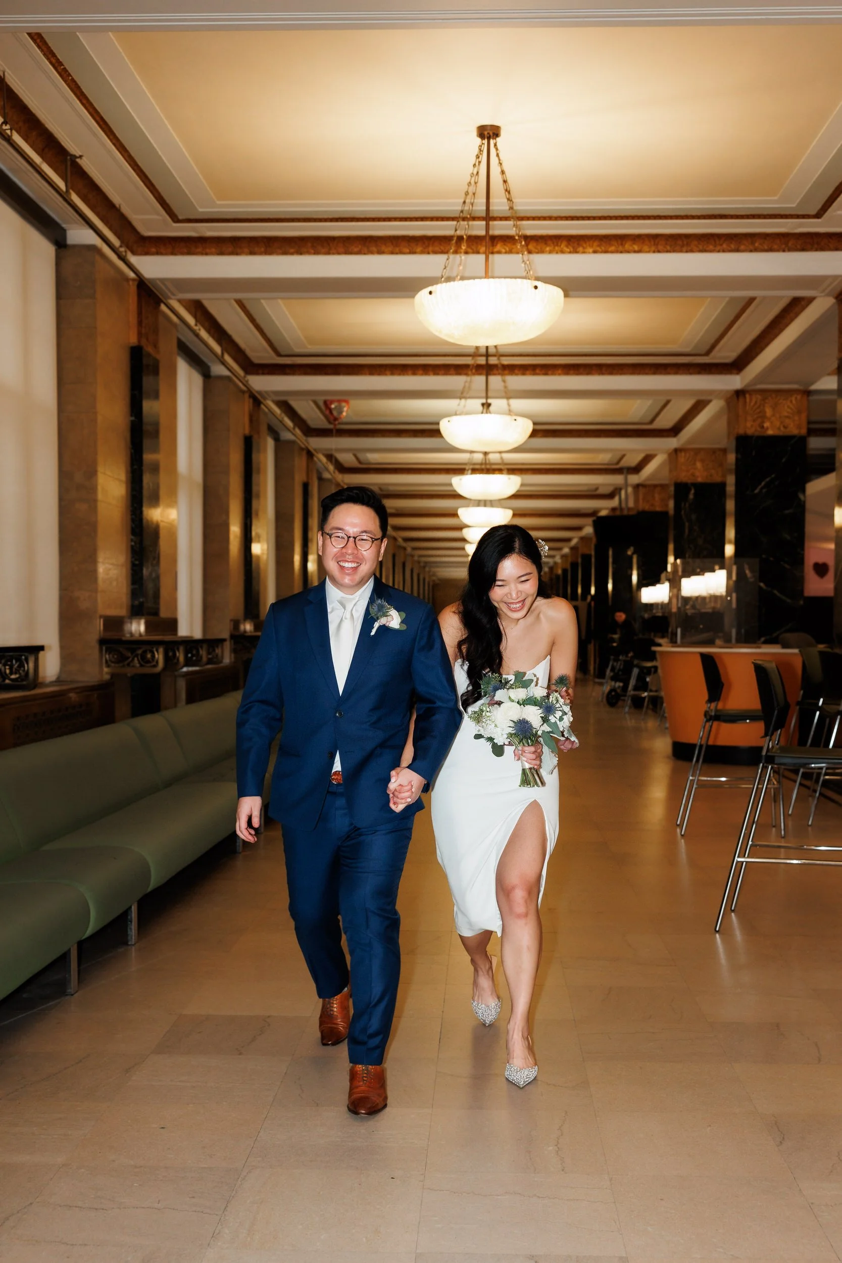 A newlywed couple laughing as they walk hand in hand in a courthouse 