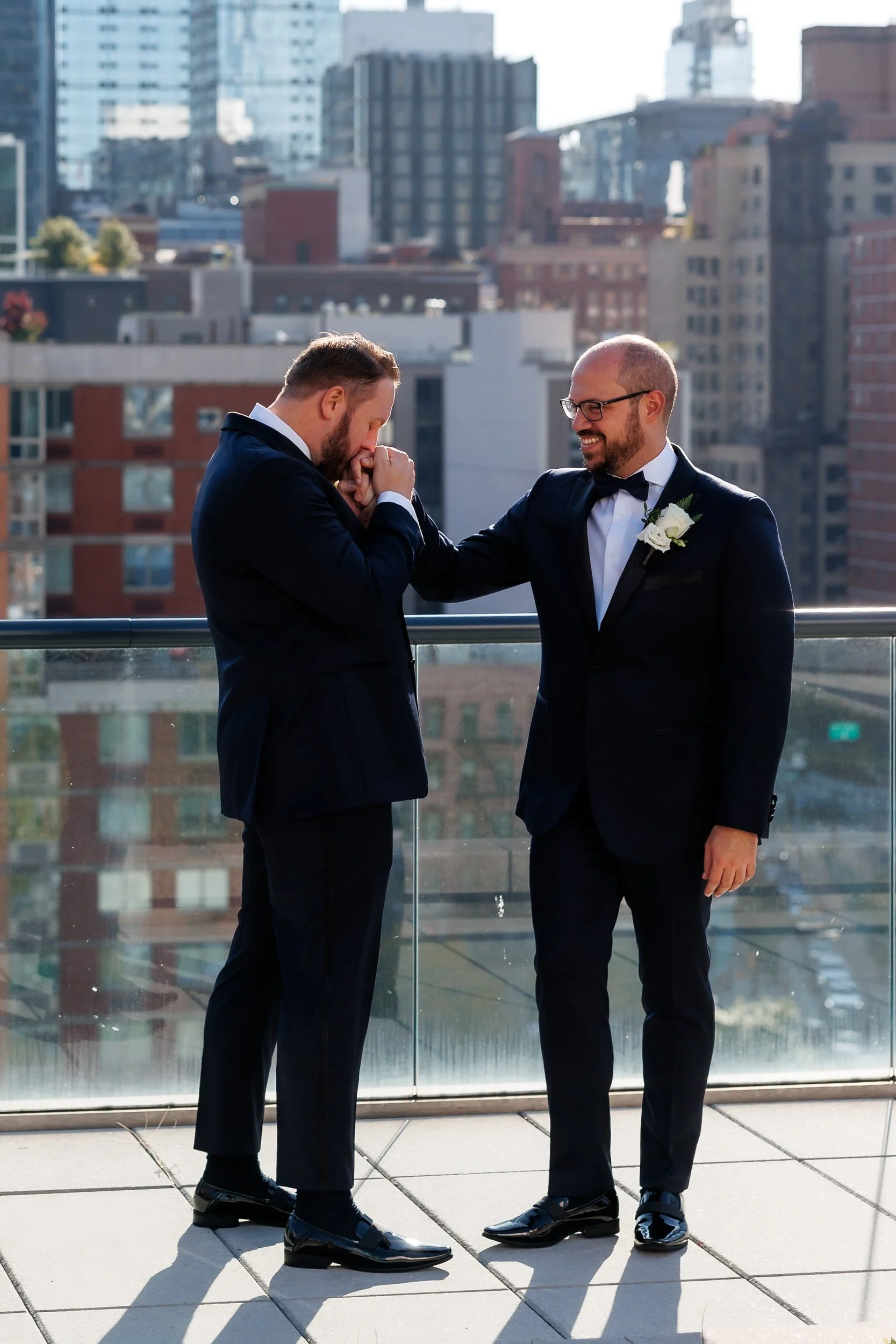 A person kissing their partner's hand as they stand on a city rooftop