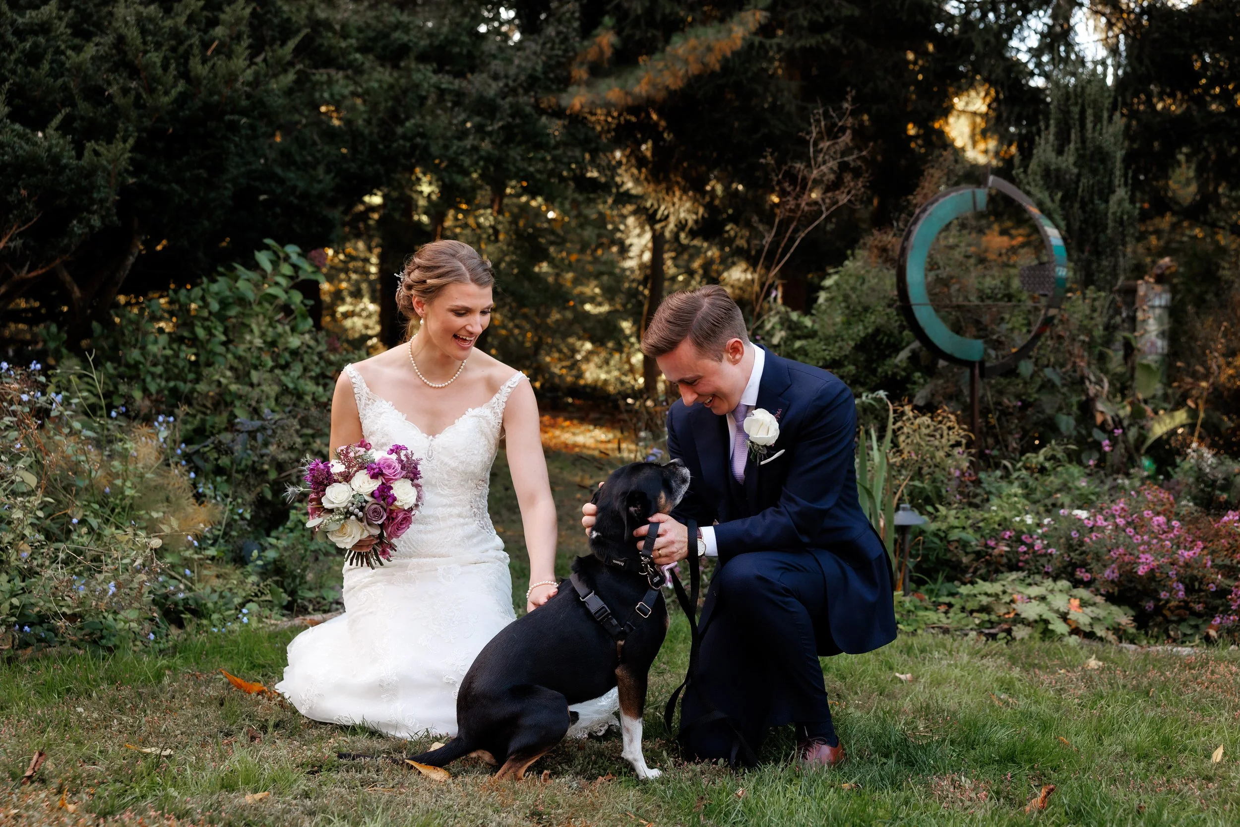 Newlyweds kneeling in the grass petting a dog 