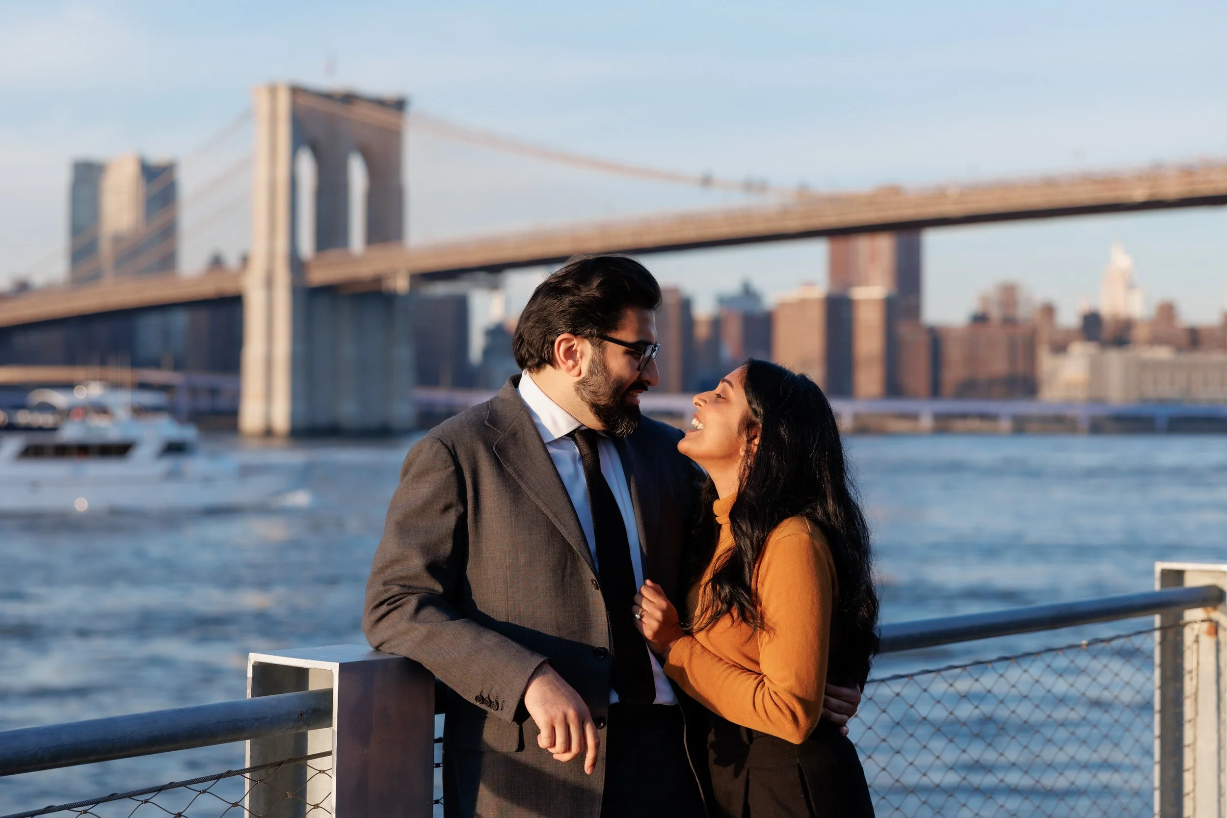 A couple leaning into each other as they stand at a railing overlooking the water 