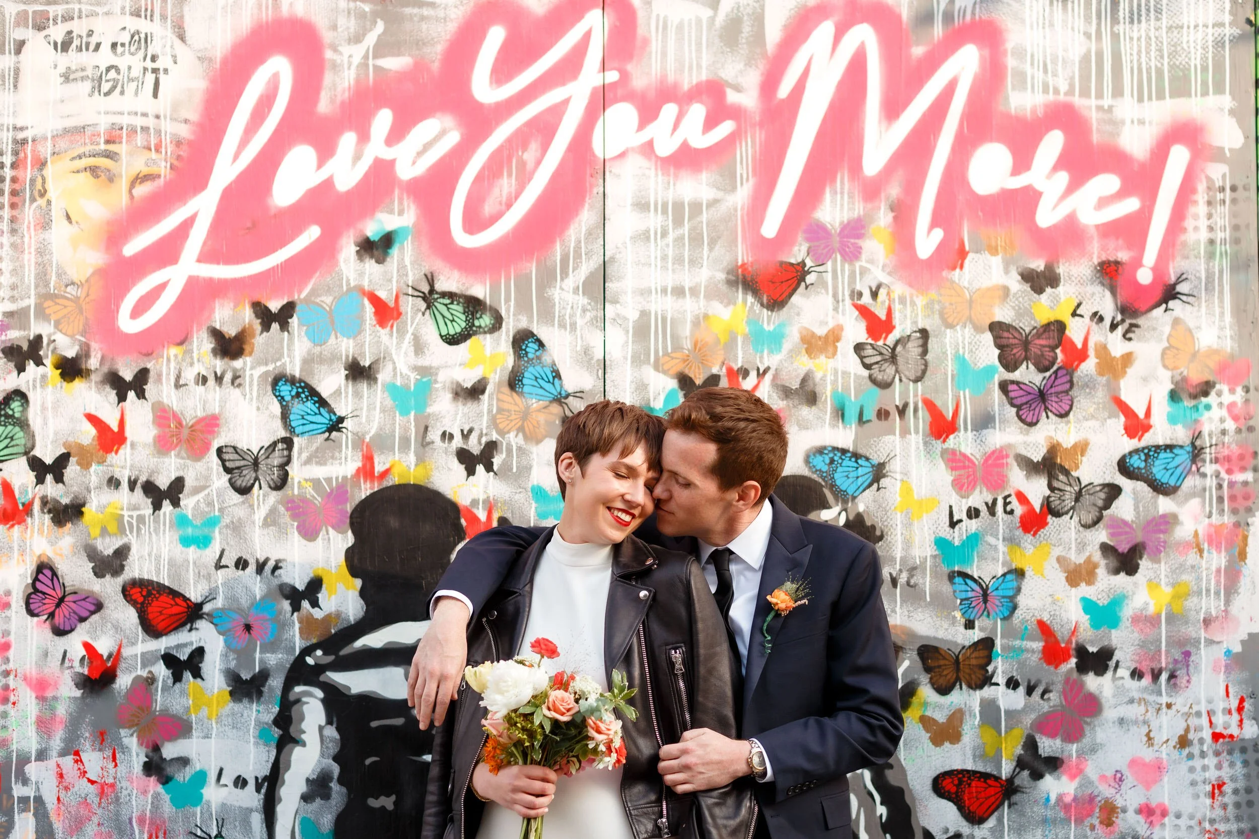 A person with their arm around their new spouse as they stand in front of a colorful mural 