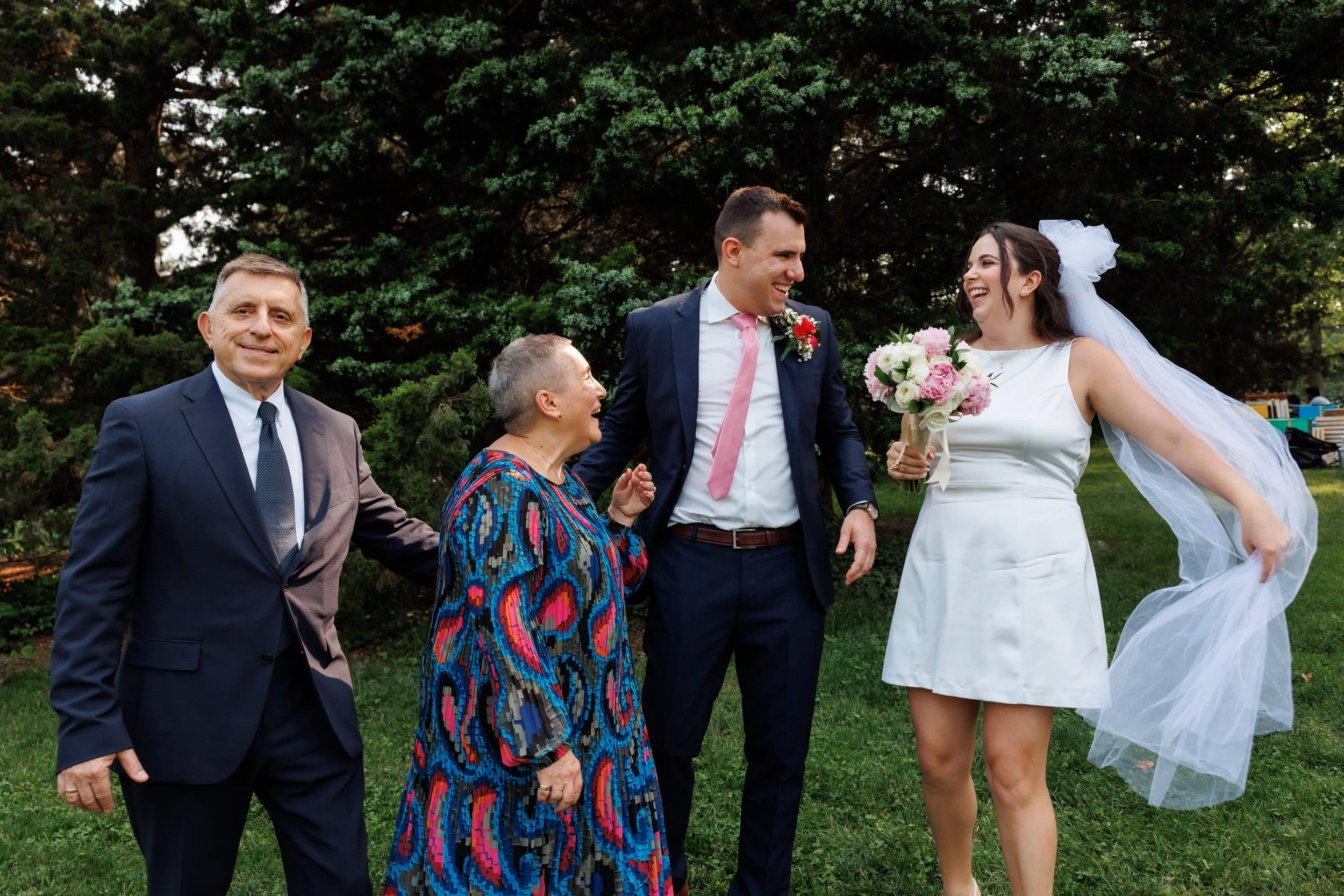 Newlyweds laughing with wedding guests as they stand outside 