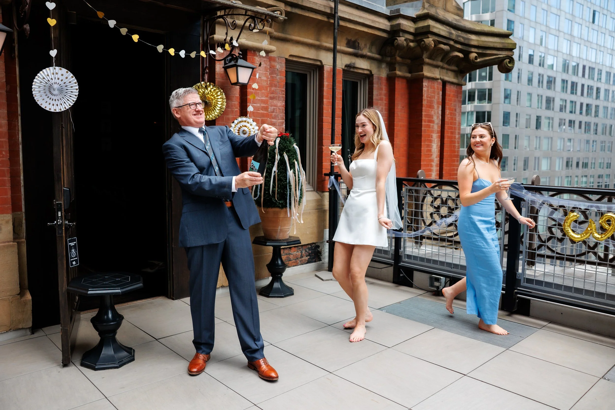 A person popping a bottle of champagne while two people laugh next to them 