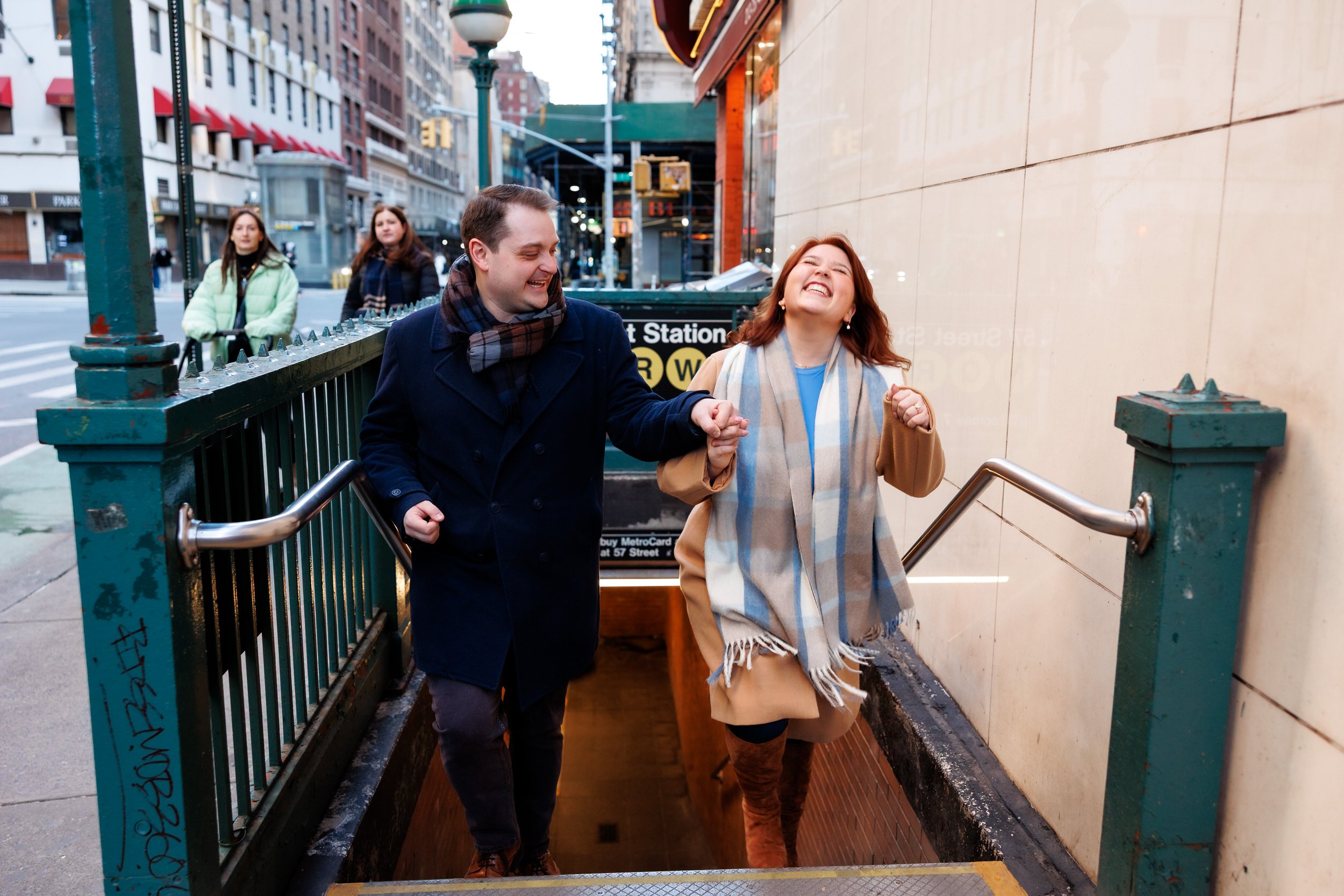 A couple laughing as they walk up the steps from a subway stop 