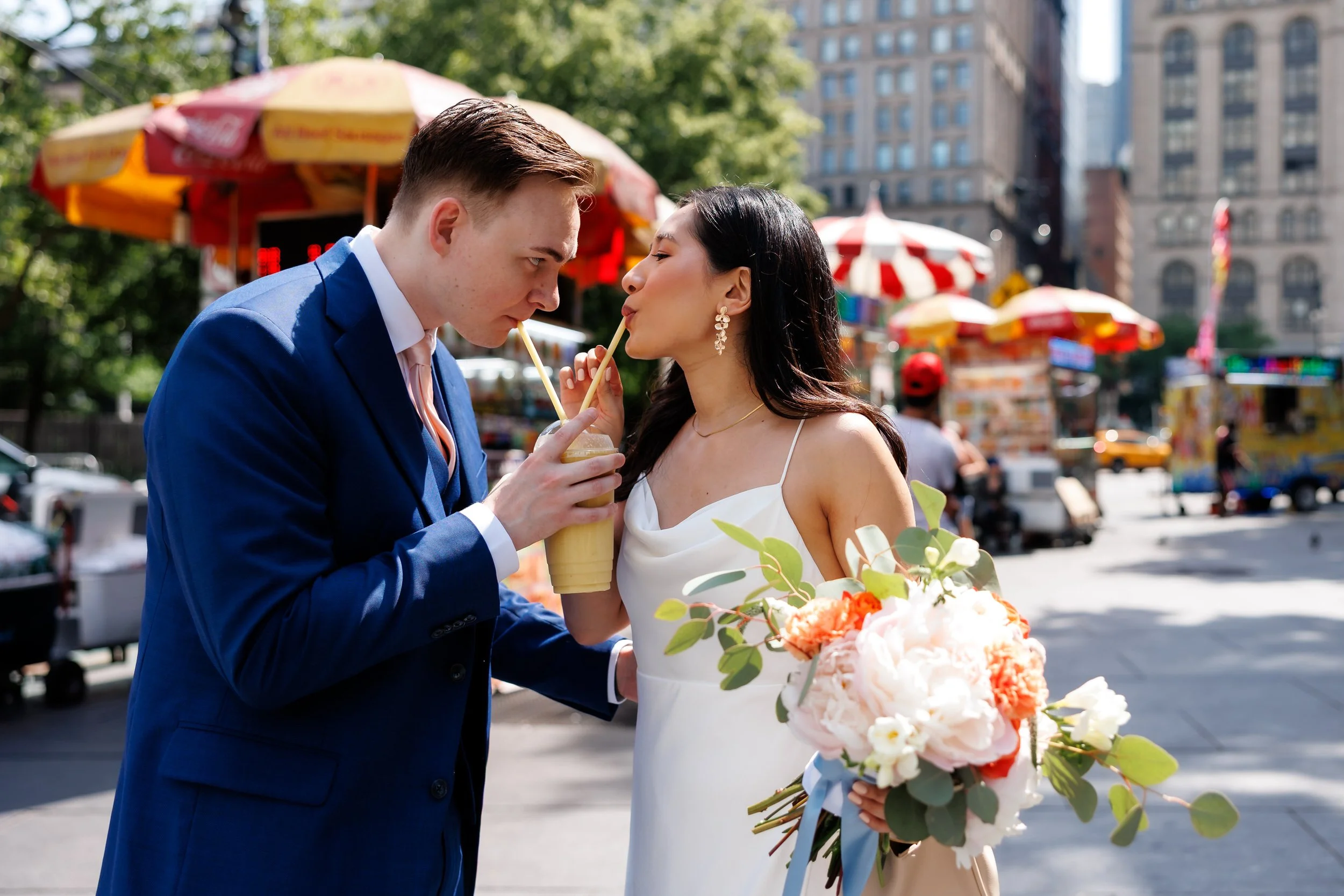 Newlyweds standing in a park drinking a milkshake together 