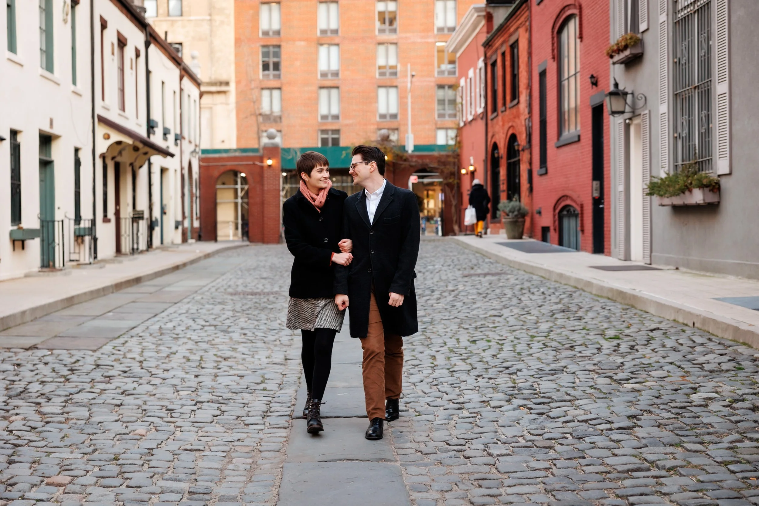 A couple walking down a cobblestone road with their arms linked 