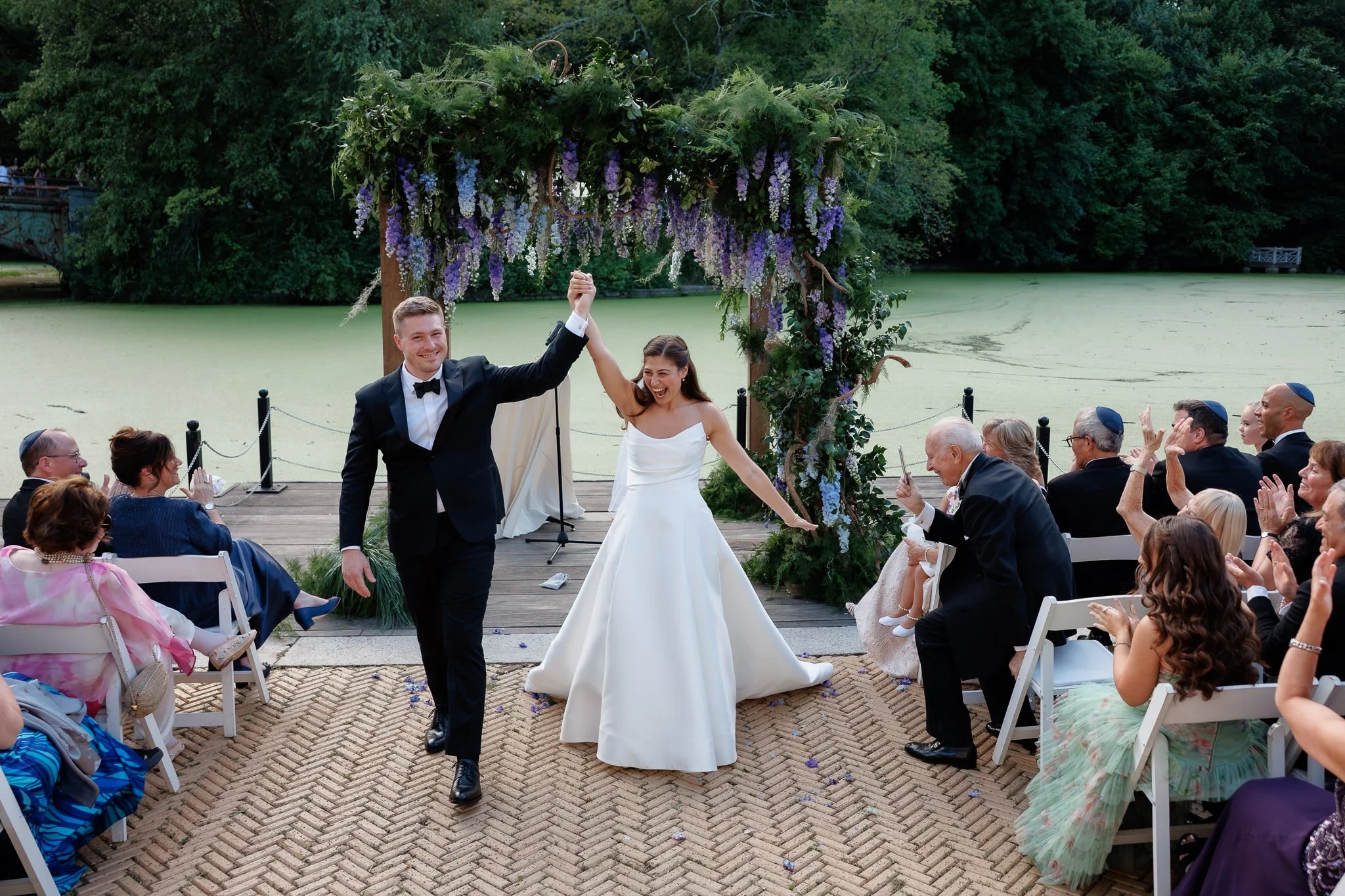 Couple raises hands in celebration as they walk back up aisle after wedding ceremony