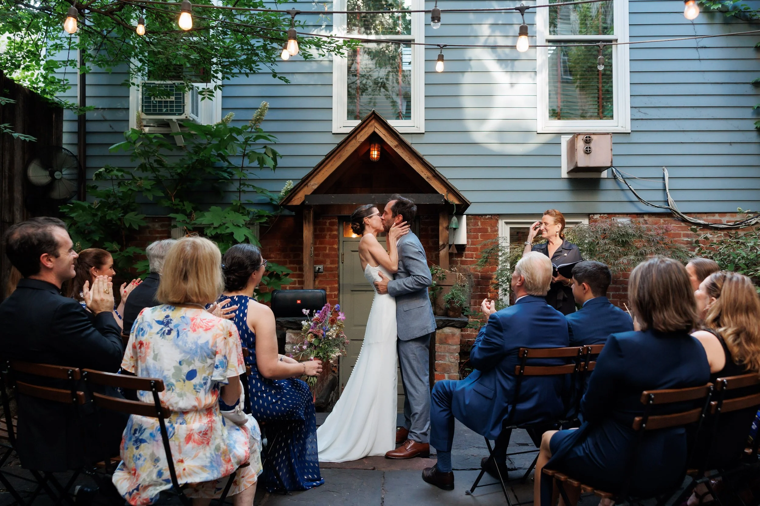 A newlywed couple during their first kiss as their guests cheer for them 