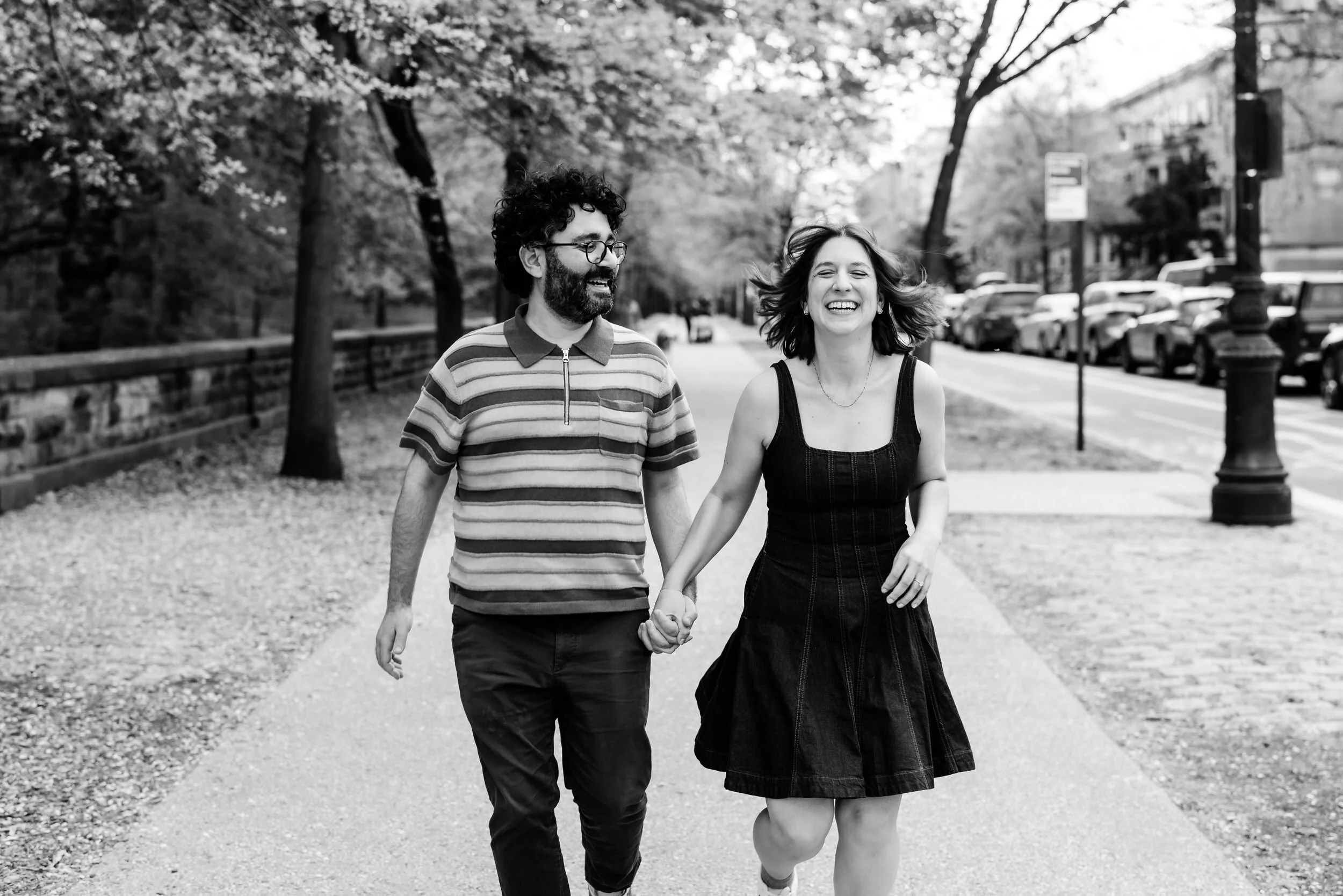 A couple holding hands and walking along a park as they laugh 