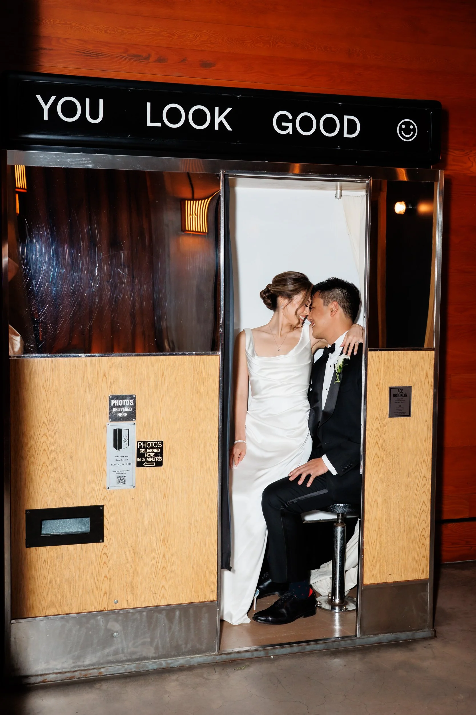 A wedding couple sitting in a small photo booth together 
