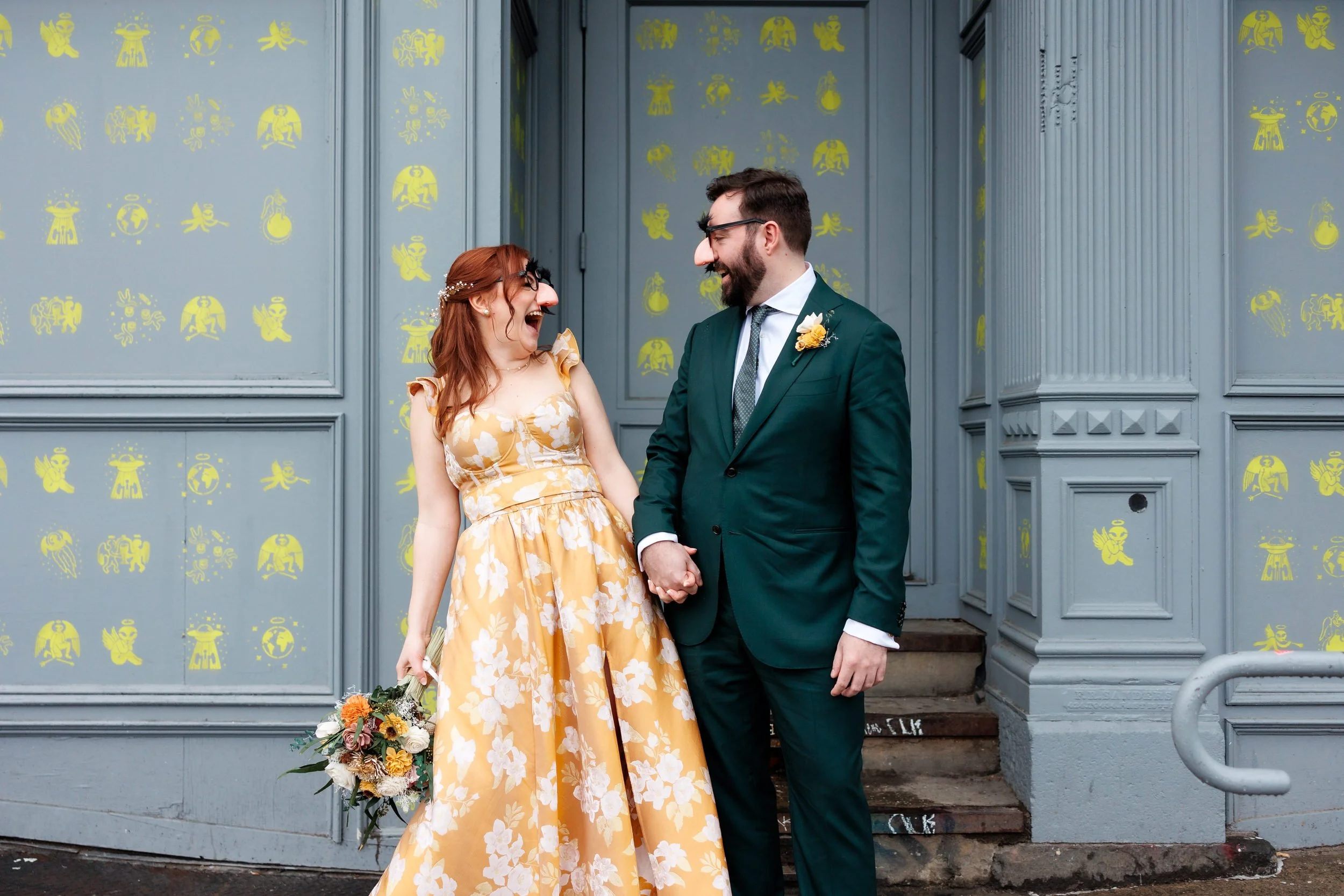 A couple holding hands and laughing as they wear glasses with fake noses and eyebrows 