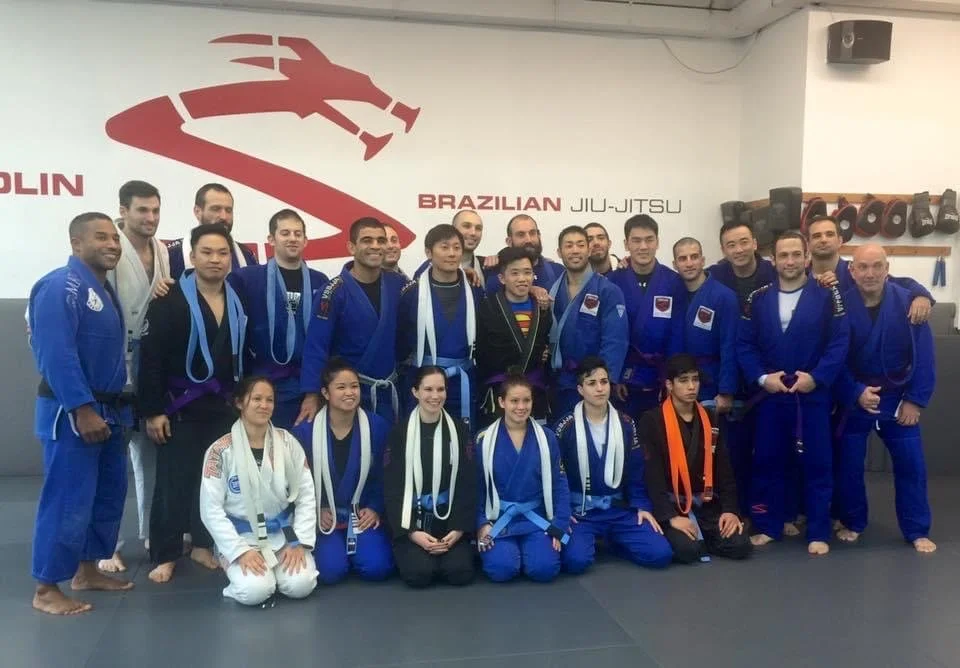 Group of people in Brazilian Jiu-Jitsu gis posing in a martial arts dojo.