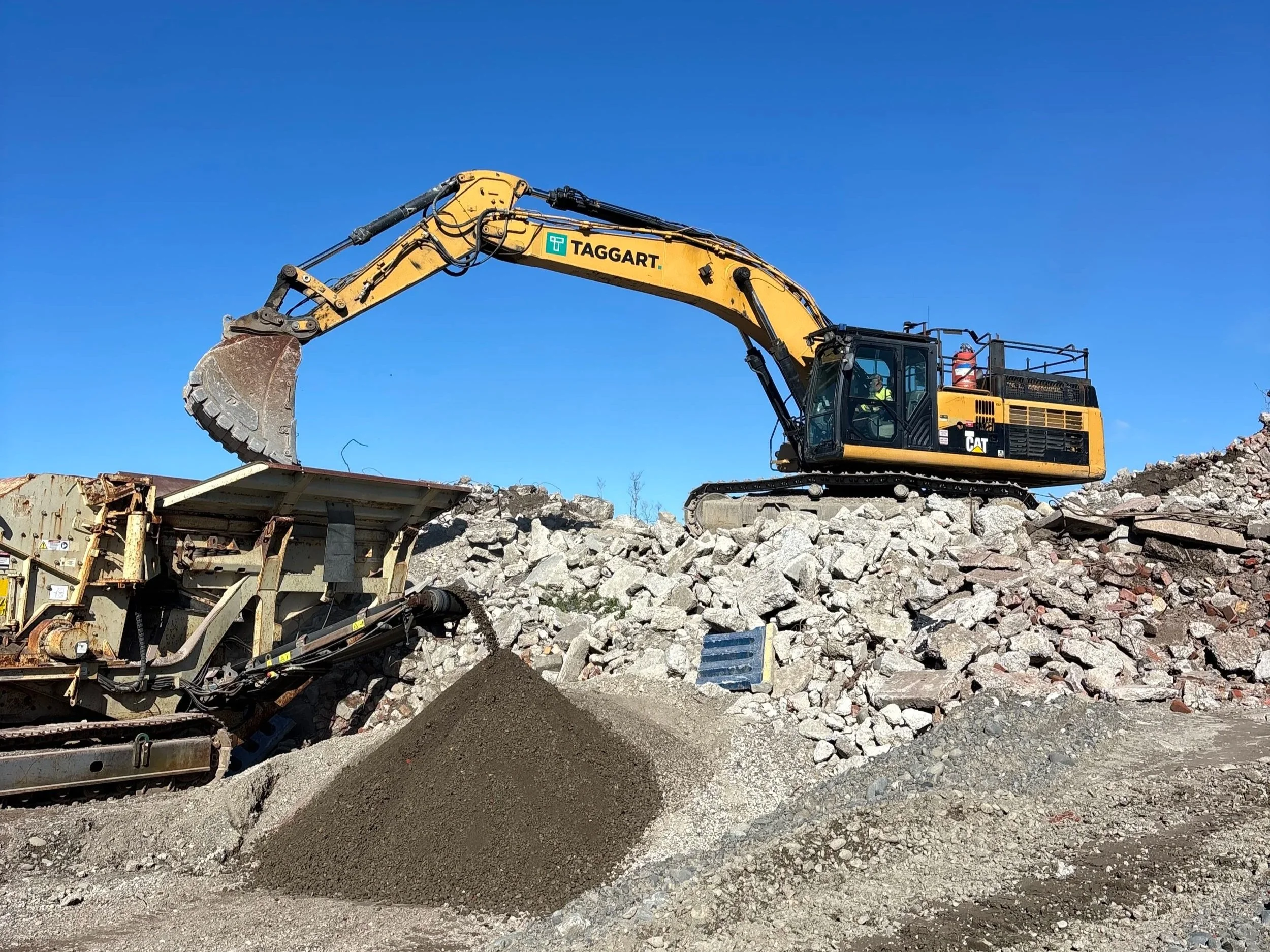 Large yellow digger putting recycled concrete into a crusher