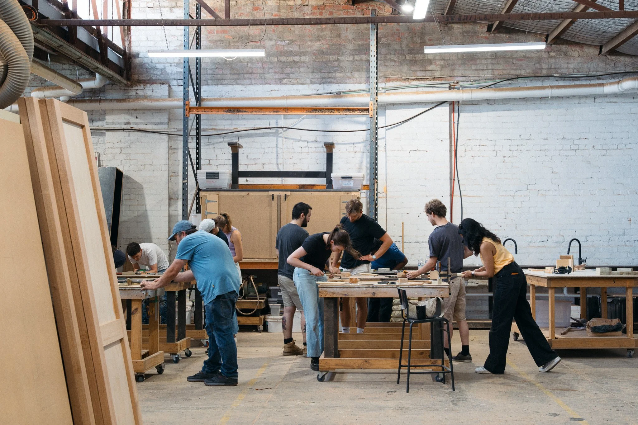 People working on woodworking projects in a woodworking studio with wooden boards and workbenches.