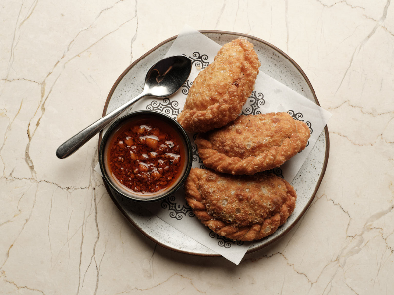Plate of three fried chicken strips with a side of spicy dipping sauce on a marble surface.