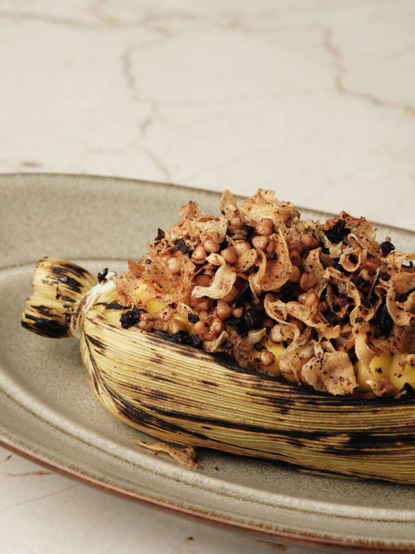 Corn cob filled with a baked stuffing mixture of corn, bread crumbs, and herbs on a beige plate.
