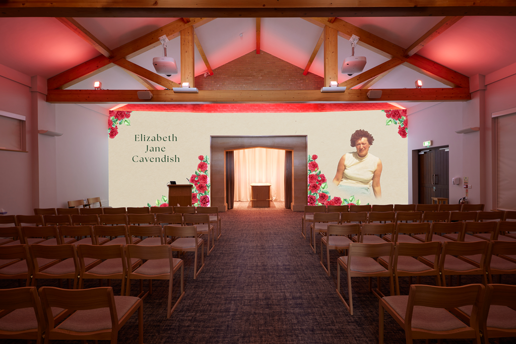 An auditorium with wooden chairs facing a large screen displaying the name Elizabeth Jane Cavendish, floral decorations, and a photo of a woman.